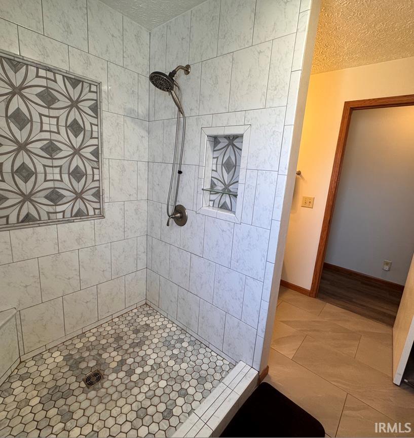 Tiled shower with a decorative mosaic inset, built-in niche with glass shelving, and a hex-tile floor