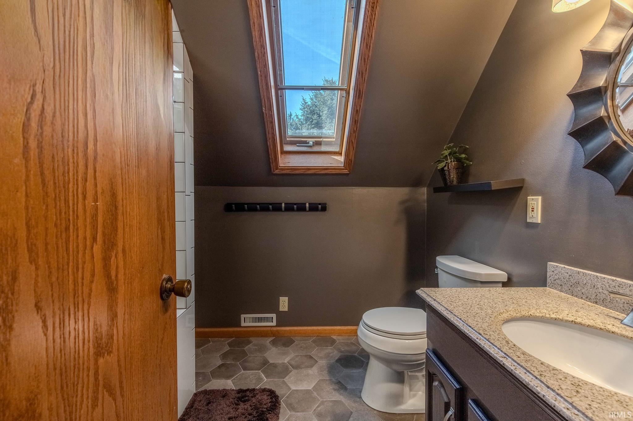 Bathroom featuring a skylight, hexagonal floor tiles, a built-in vanity with a composite countertop, and a wall-mounted mirror
