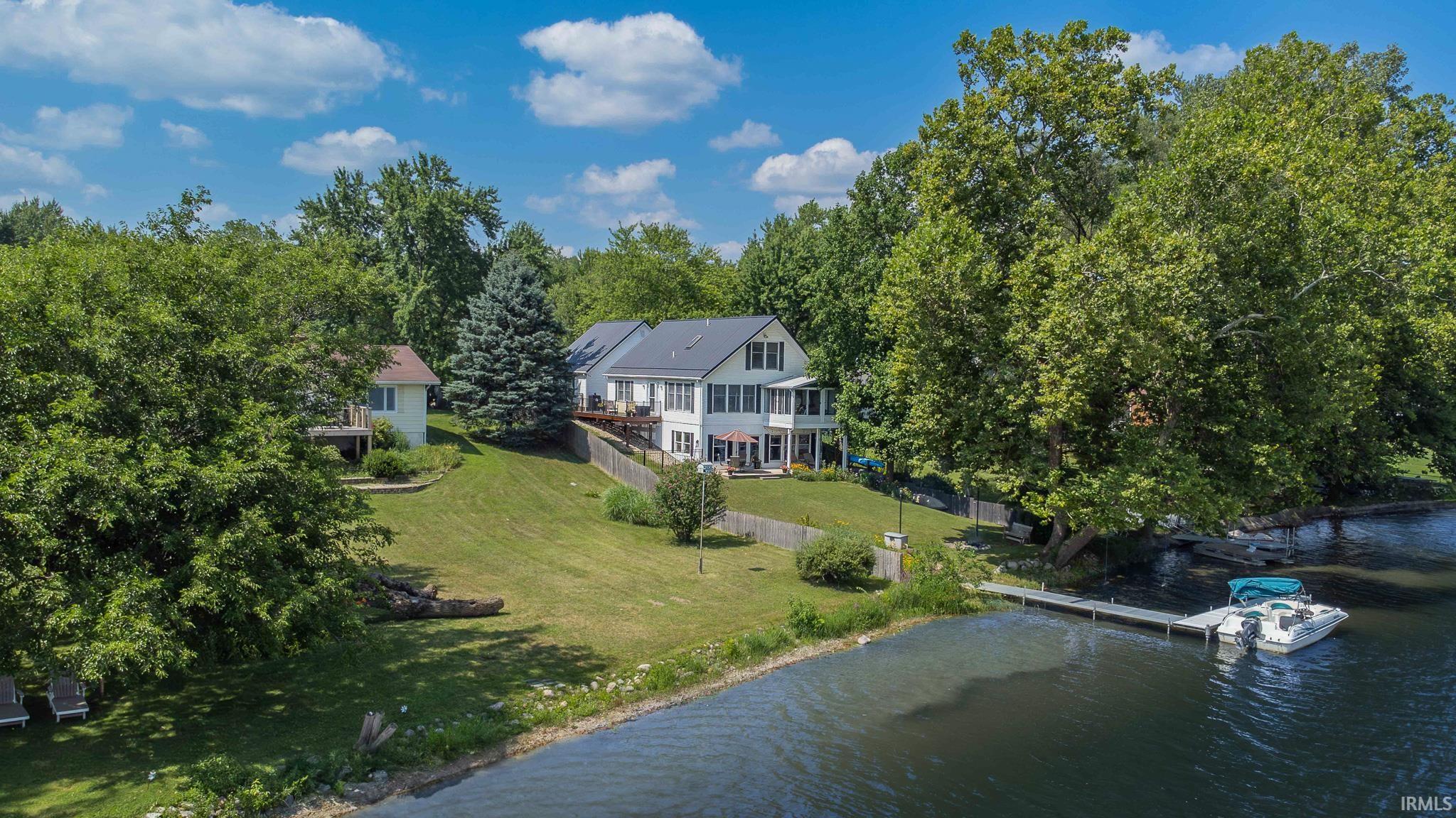 Lakeside residence featuring a multi-story exterior, an expansive terraced lawn, and mature trees