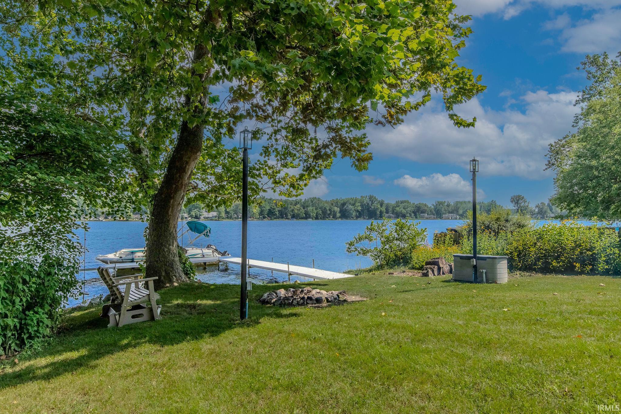 Lakefront property featuring a private dock, mature trees, and a spacious green lawn
