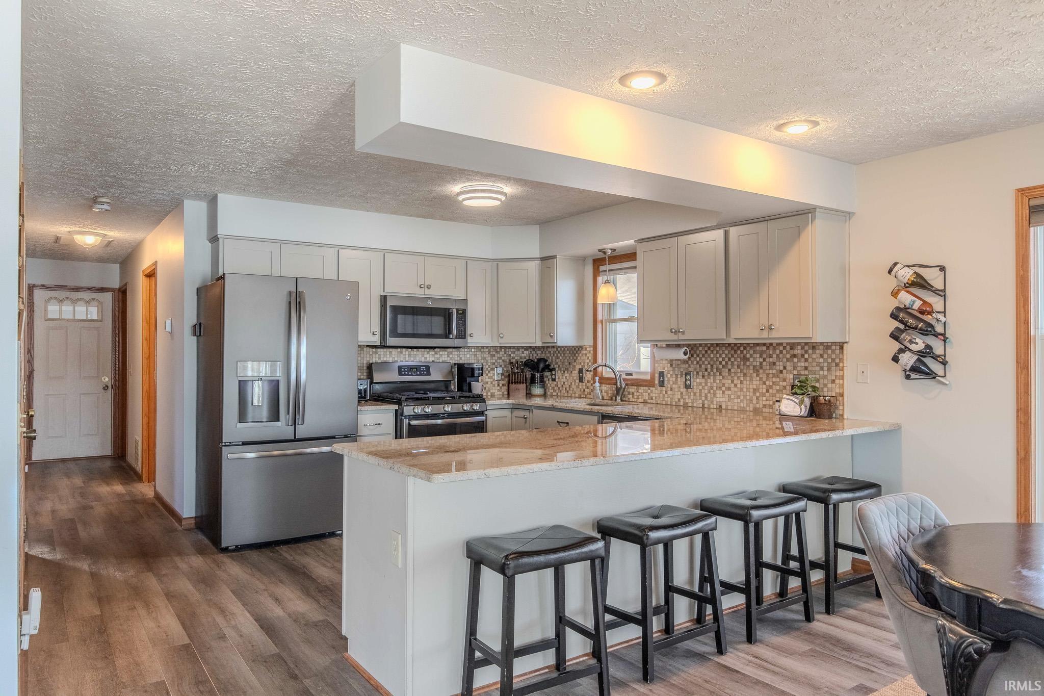 Modern kitchen featuring light cabinetry, stainless steel appliances, a mosaic tile backsplash, and a breakfast bar with stone-finish countertops