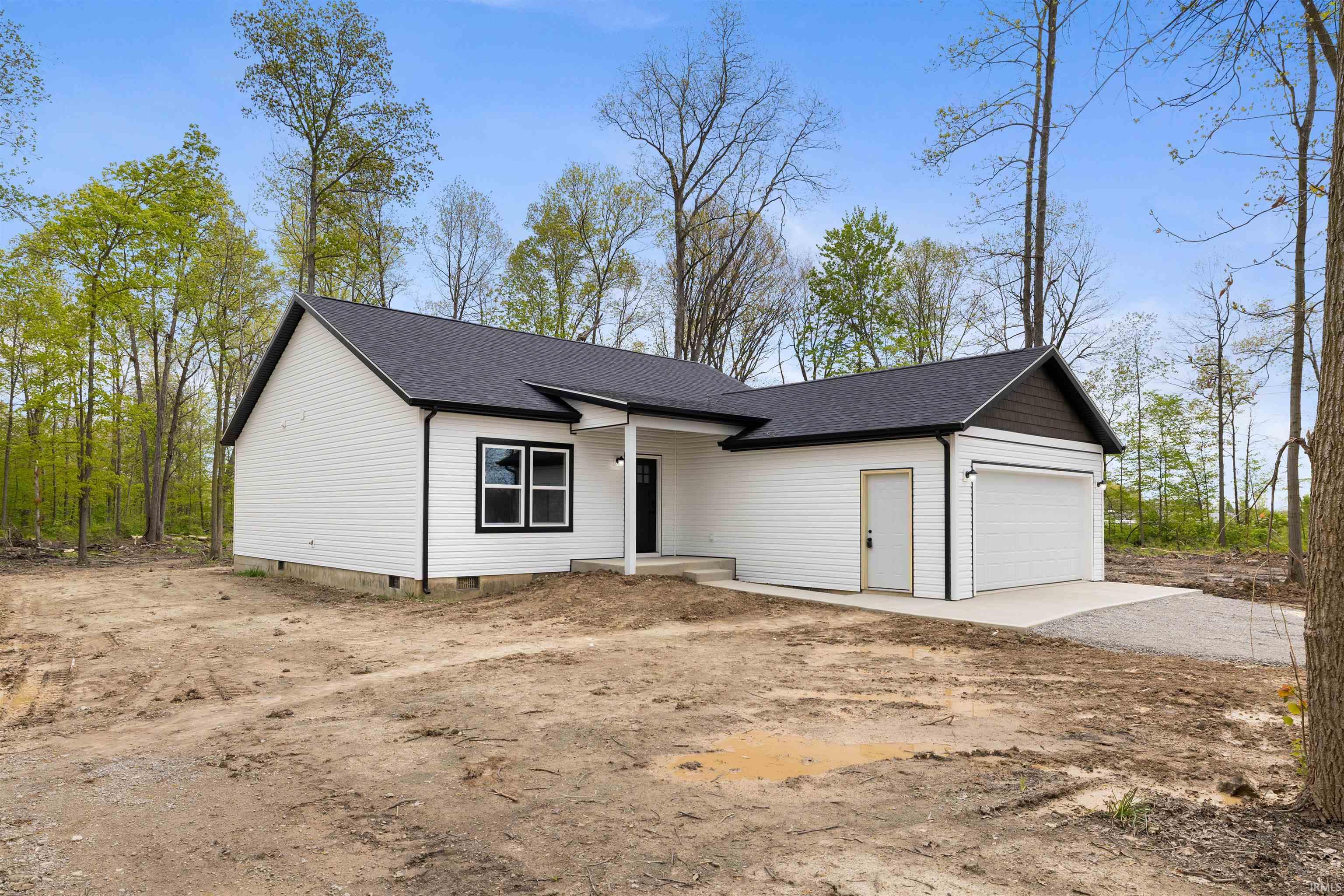 Contemporary ranch-style residence featuring white siding, a dark shingle roof, black window trim, a covered front entry, and an attached two-car garage with a side access door