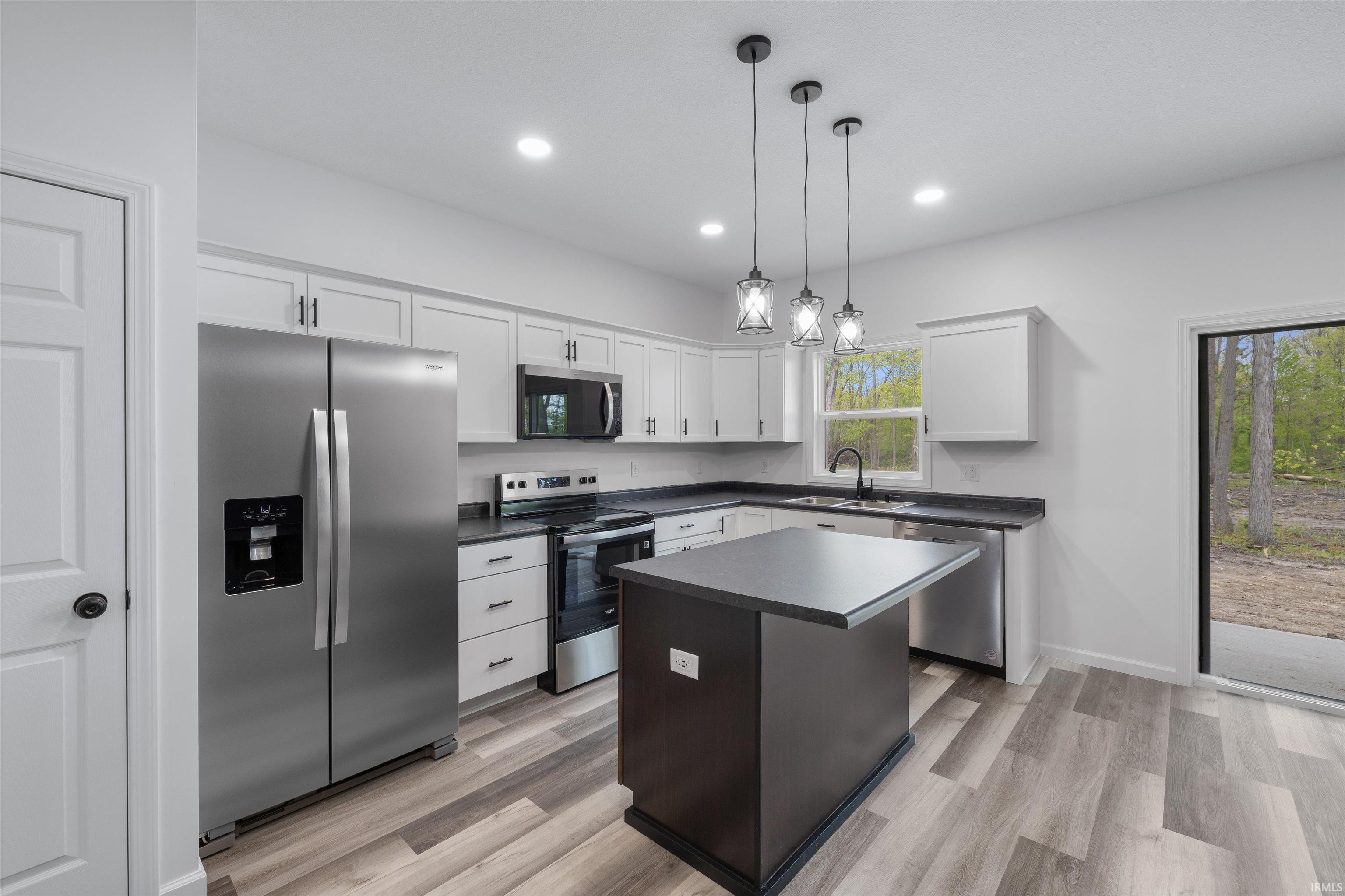 Modern kitchen featuring stainless steel appliances, light cabinetry, dark countertops, and wood-finish flooring