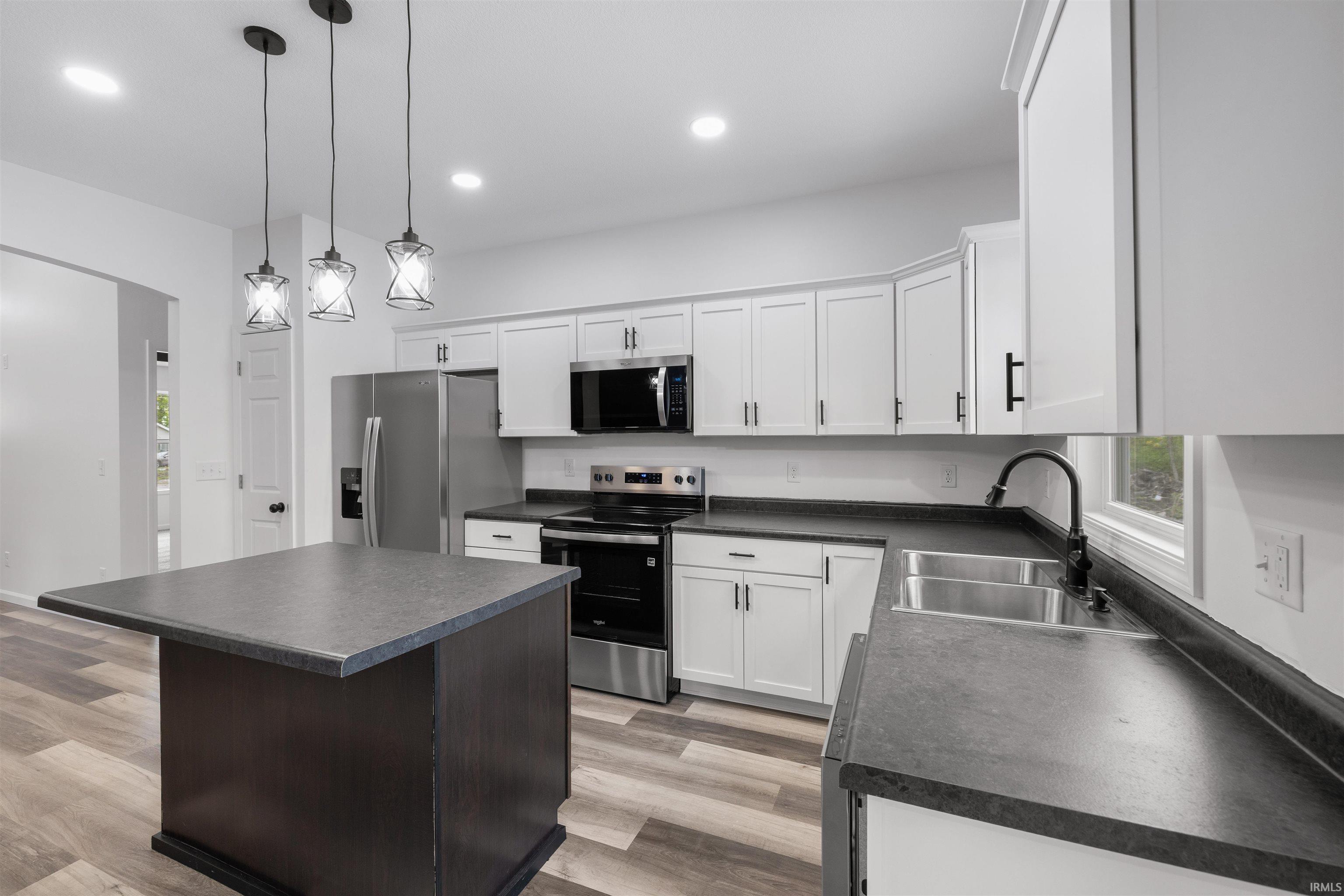 Modern kitchen featuring white cabinetry, dark countertops, stainless steel appliances, a center island, and wood-finish flooring