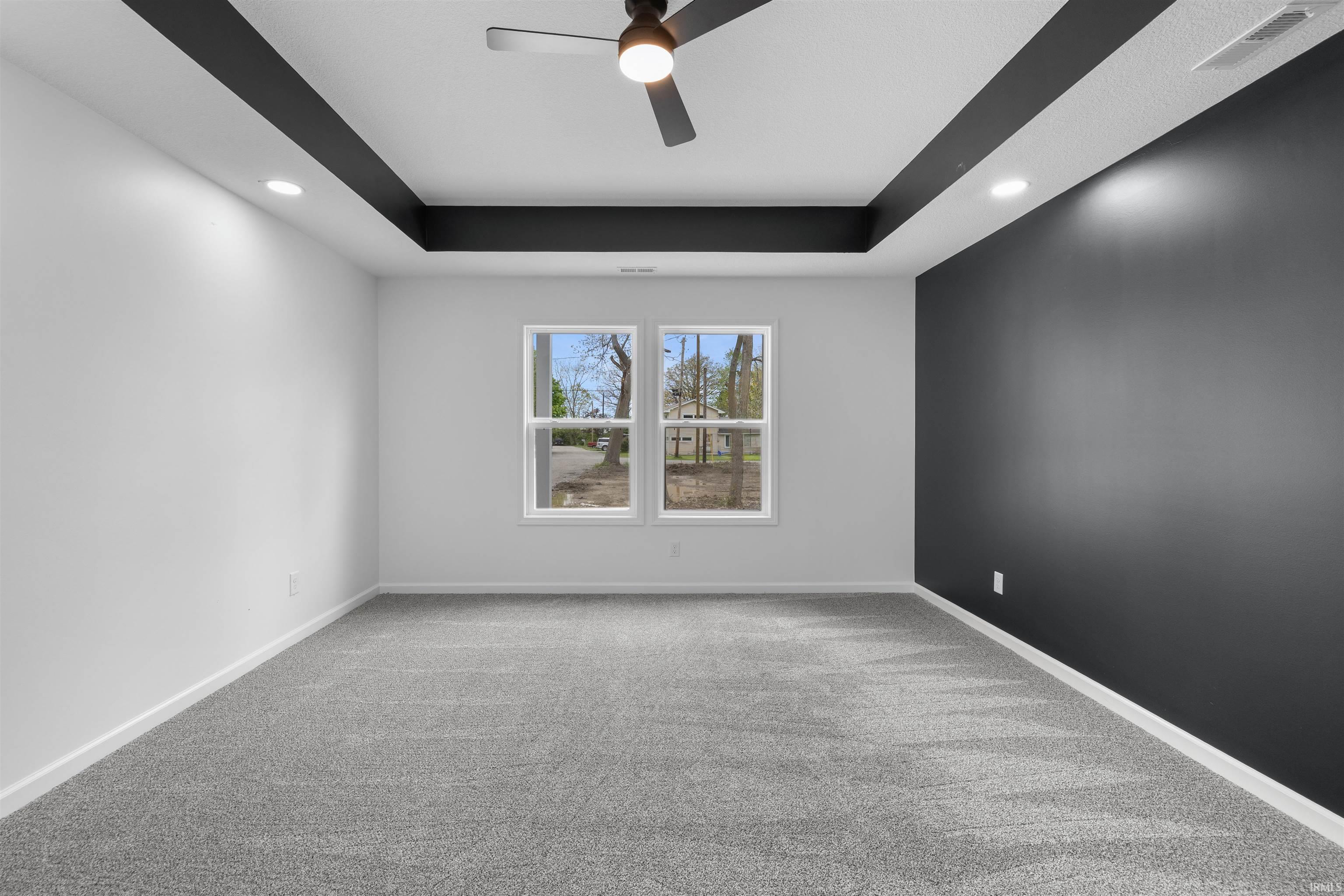 Spacious room featuring a tray ceiling with dark accents, recessed lighting, and a ceiling fan