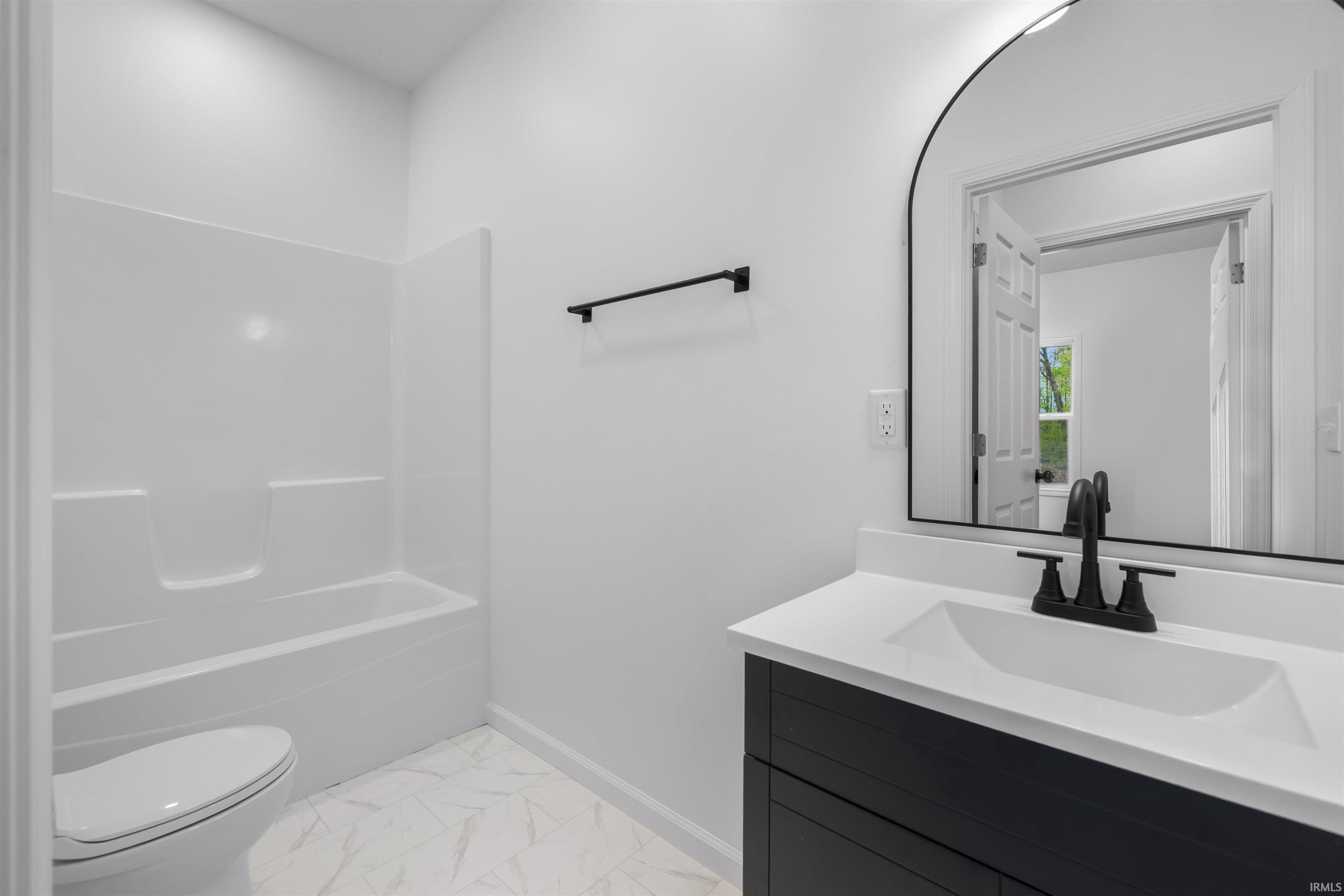 Bathroom featuring a white bathtub/shower combination, a black vanity with a white integrated sink, a matte black faucet, and an arched mirror with a black frame