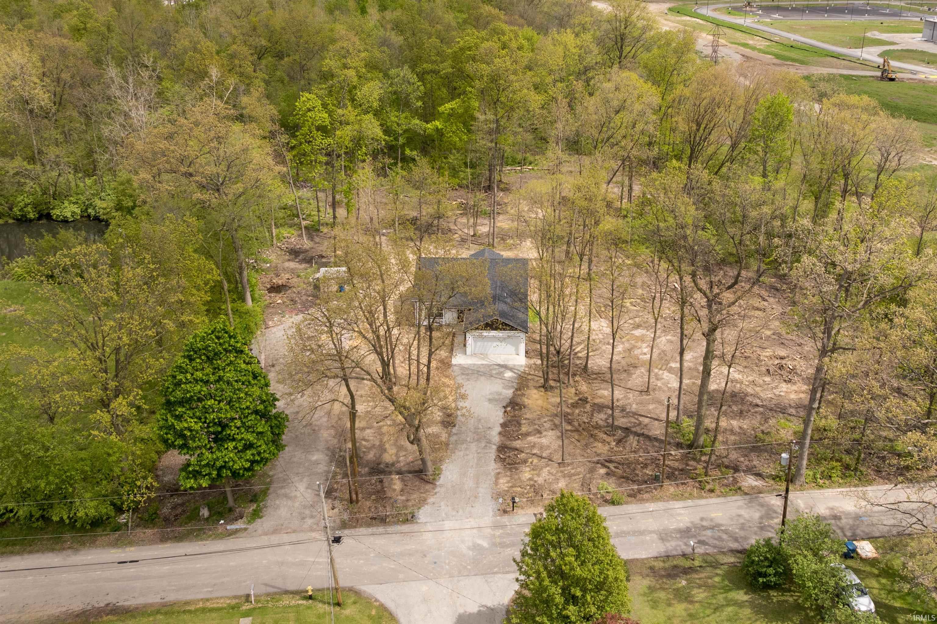 Property featuring a central residence, a gravel driveway, and a partially cleared wooded lot