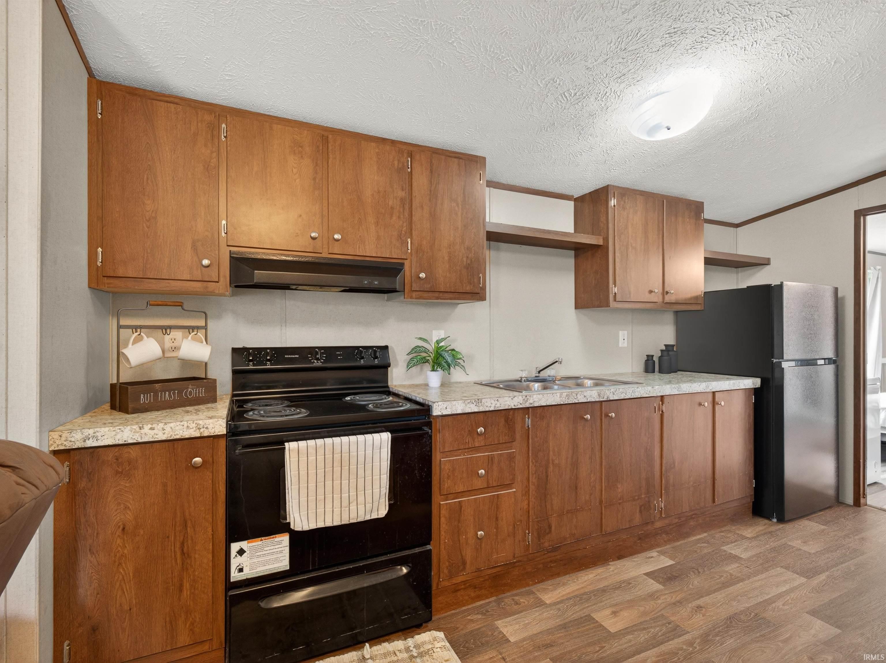 Kitchen featuring wood-finish cabinetry, solid surface countertops, a stainless steel sink, a black electric range, and wood-finish flooring