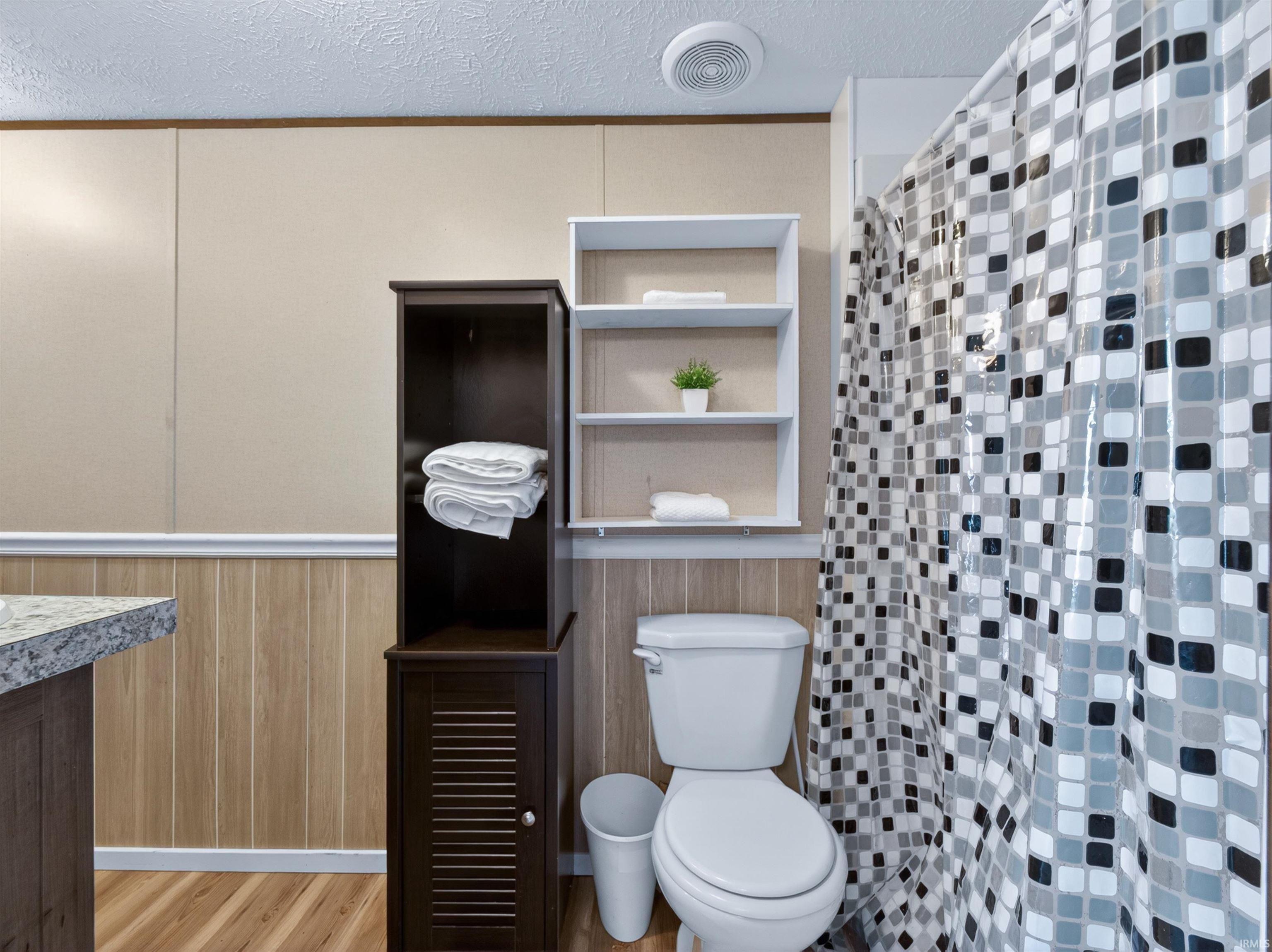 Bathroom featuring a toilet, built-in shelving, and wood-finish flooring