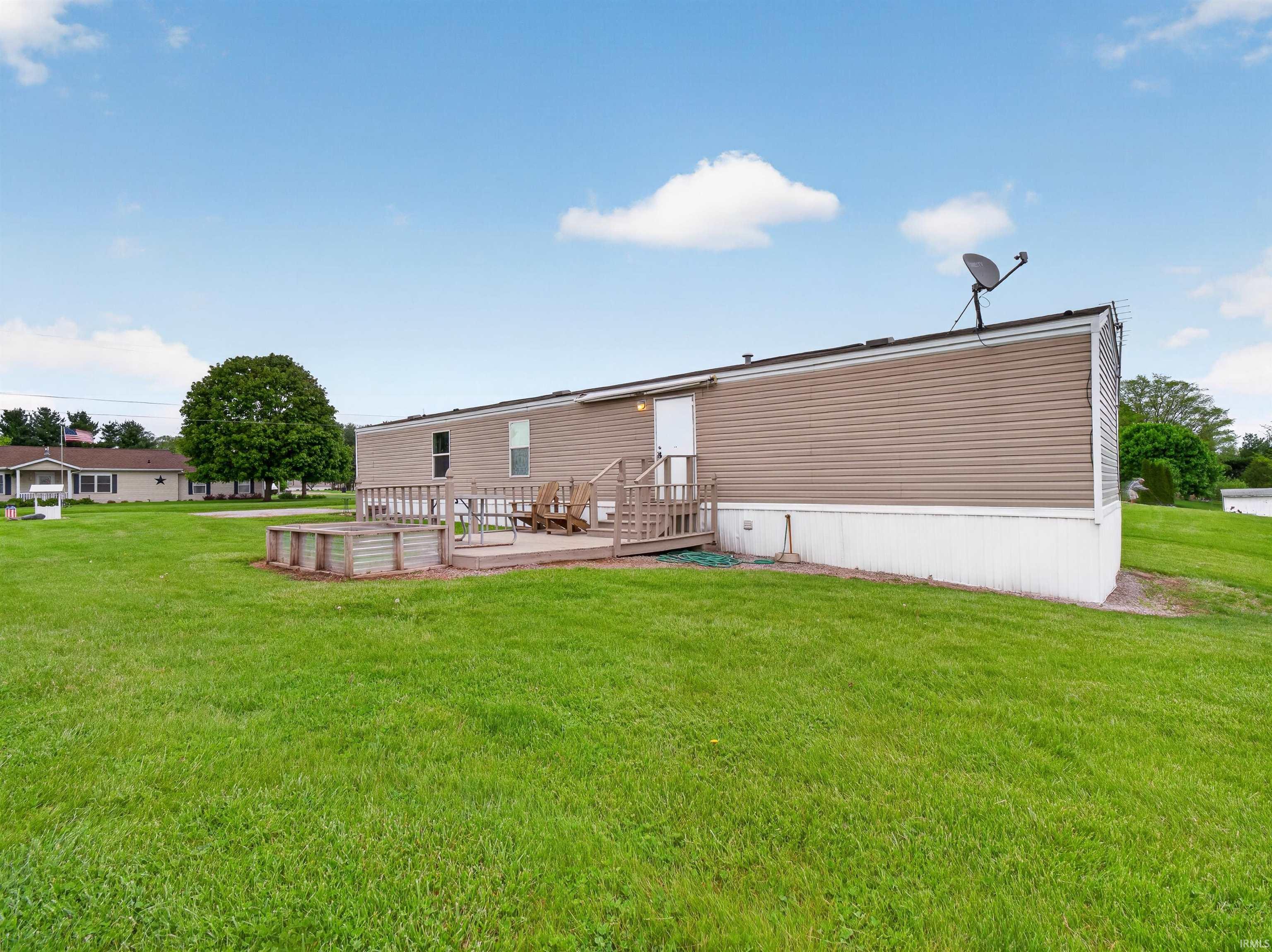 Expansive green lawn surrounds the property, featuring a raised deck with wood railing