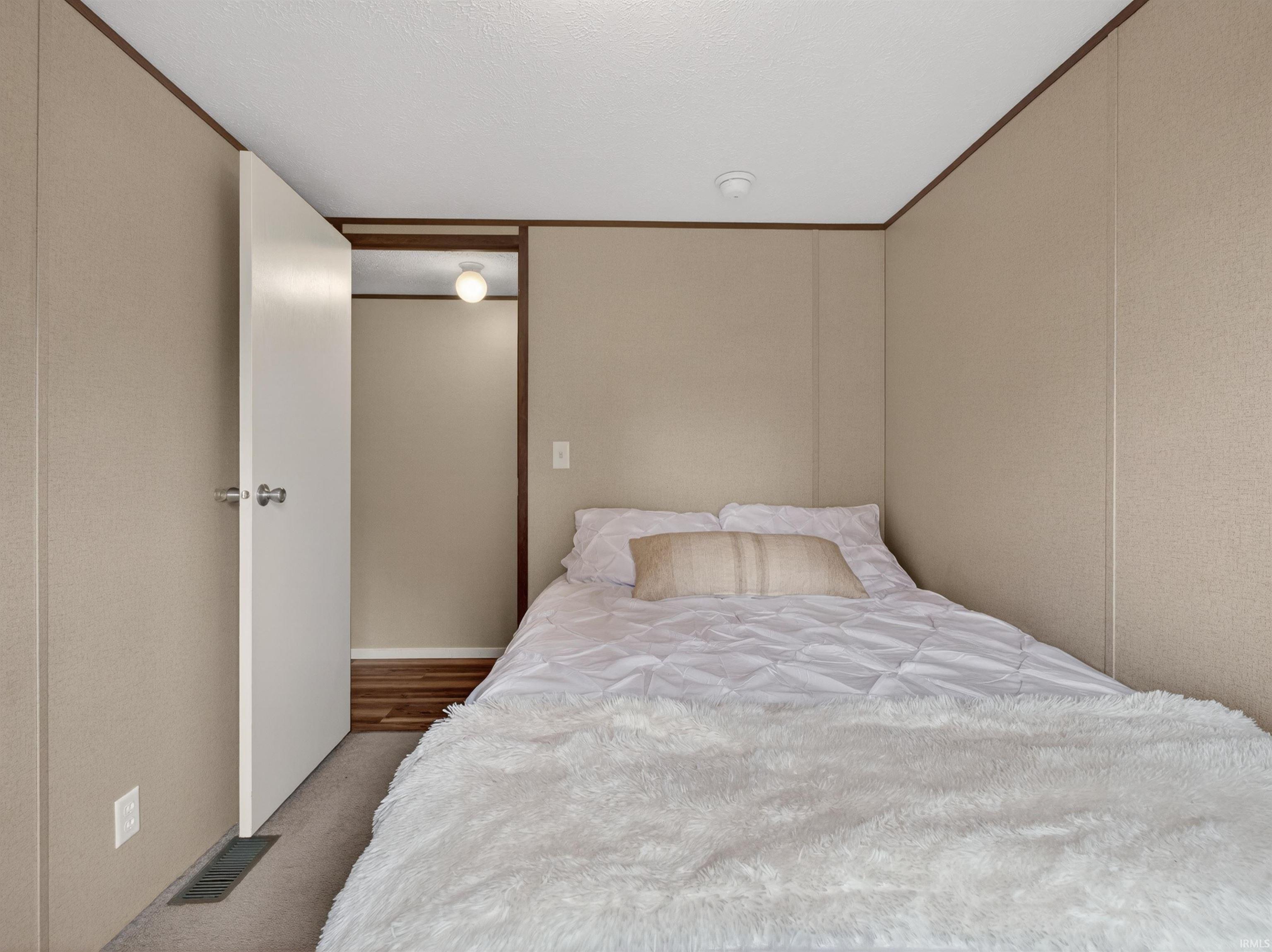 Compact room featuring neutral-toned walls, contrasting brown trim, and a partially open doorway revealing wood-finish flooring
