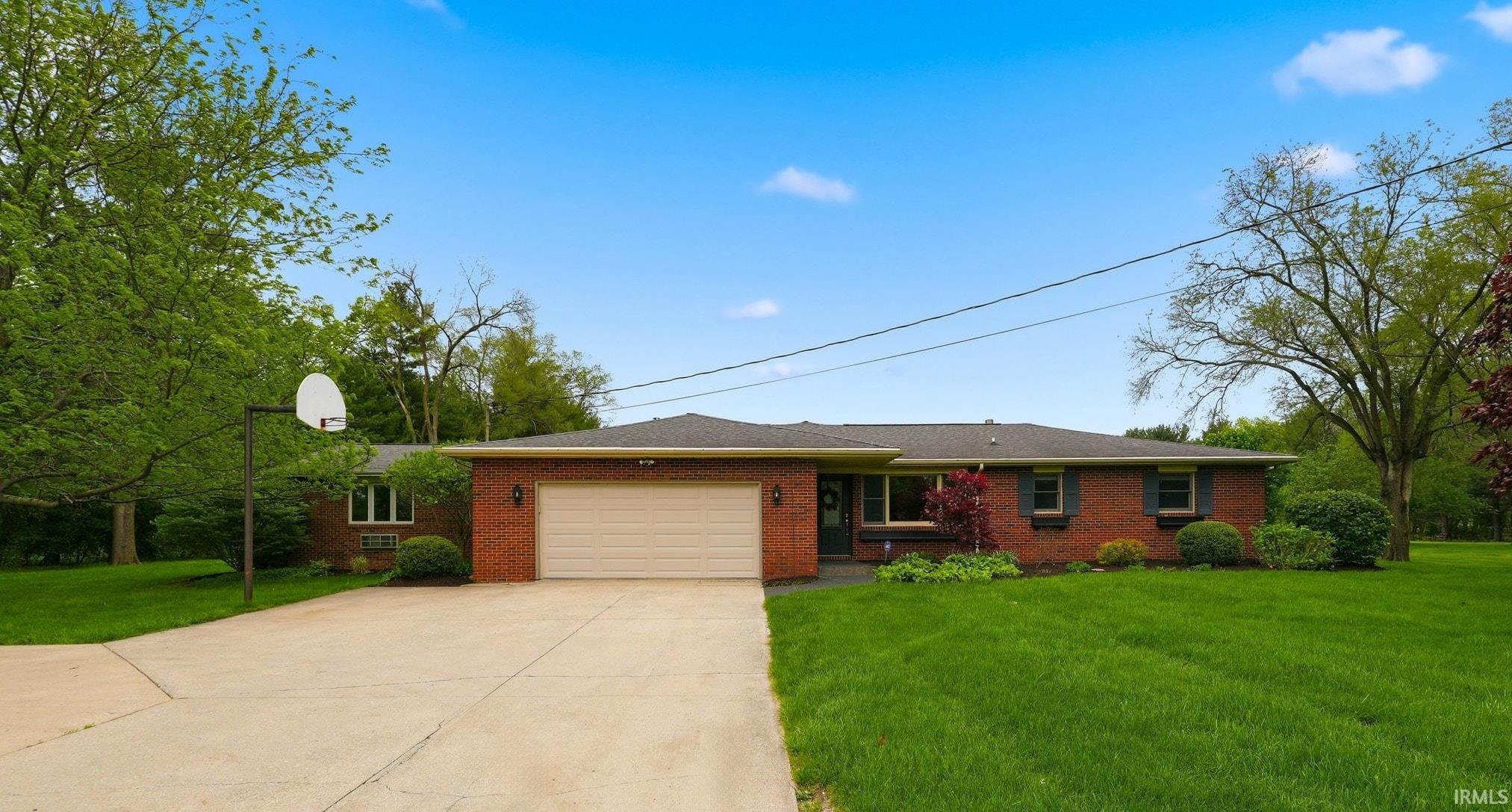 Brick ranch-style residence featuring an attached two-car garage with a light-colored garage door, a concrete driveway, and a basketball hoop