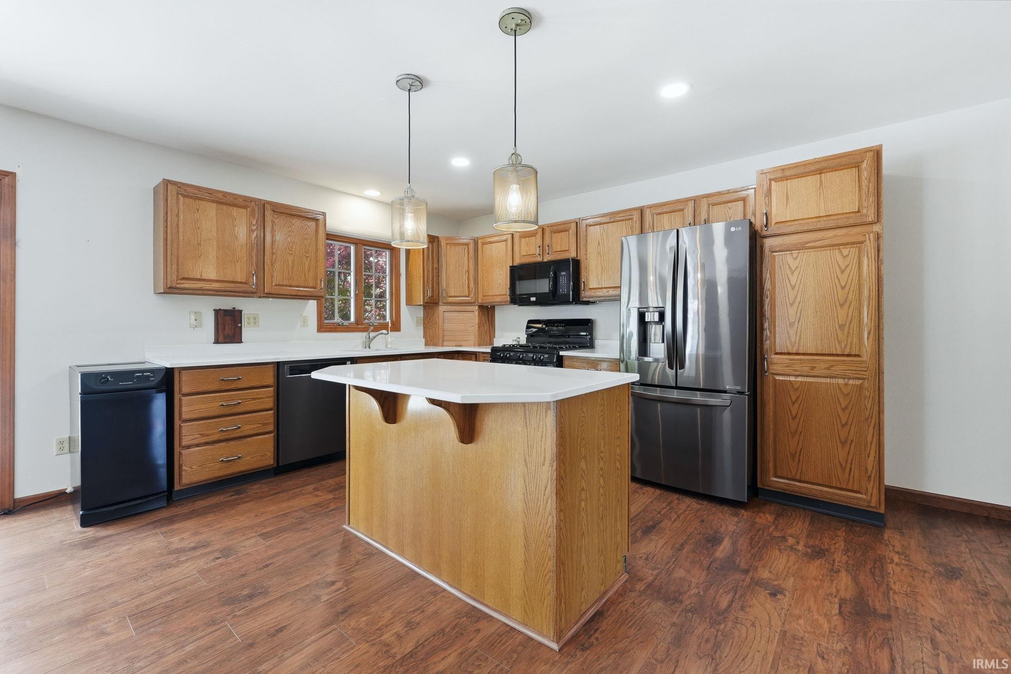 Kitchen featuring wood-finish flooring, wood cabinetry, white countertops, a central island with a white countertop, and stainless steel appliances