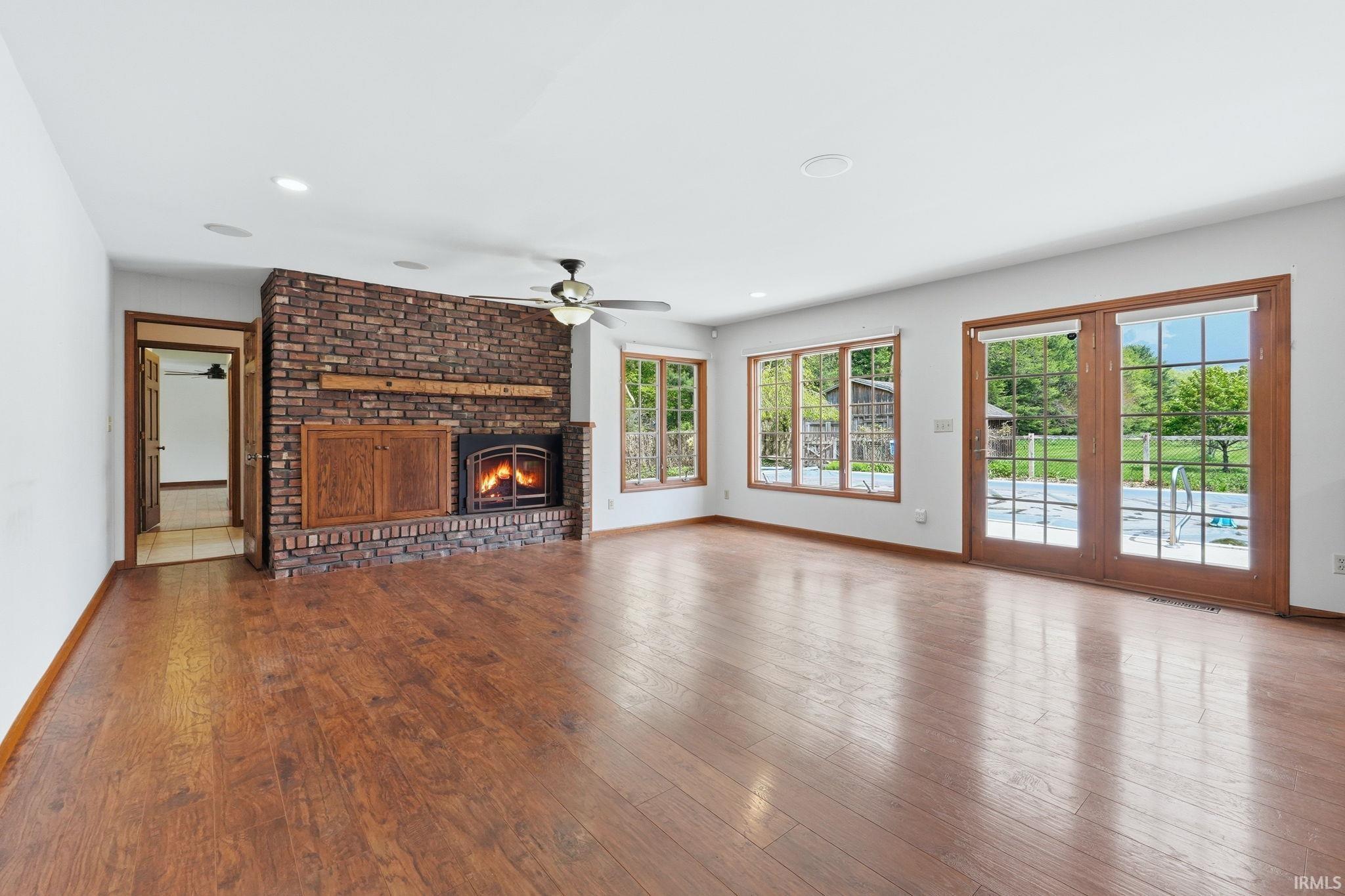 Spacious room featuring wood-finish flooring, a brick fireplace with wood mantel and built-in cabinetry, and multiple windows with wood trim