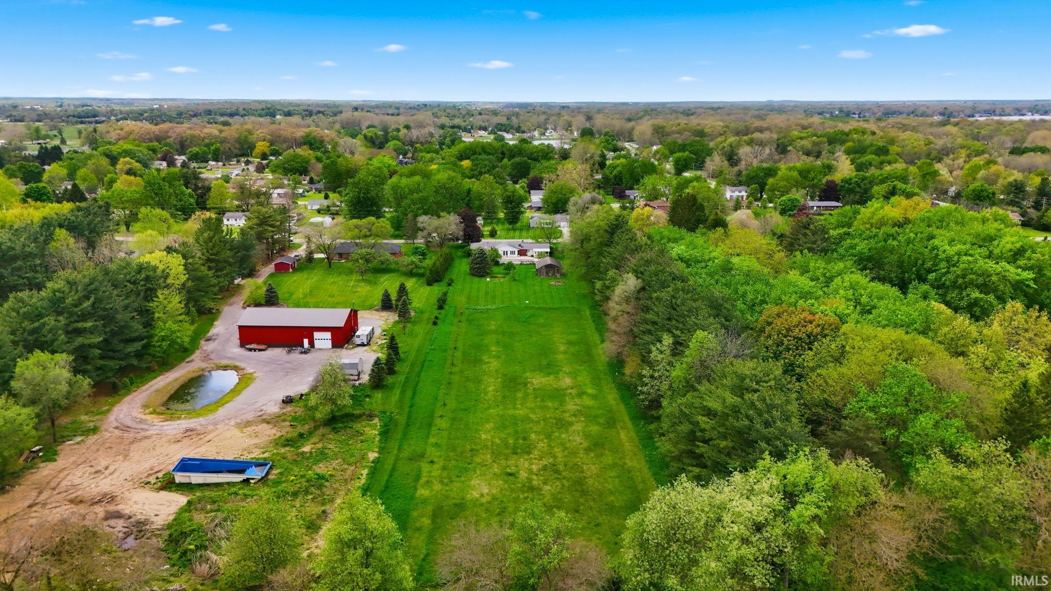 Expansive green lot featuring a long, manicured lawn bordered by mature trees and a substantial red barn structure