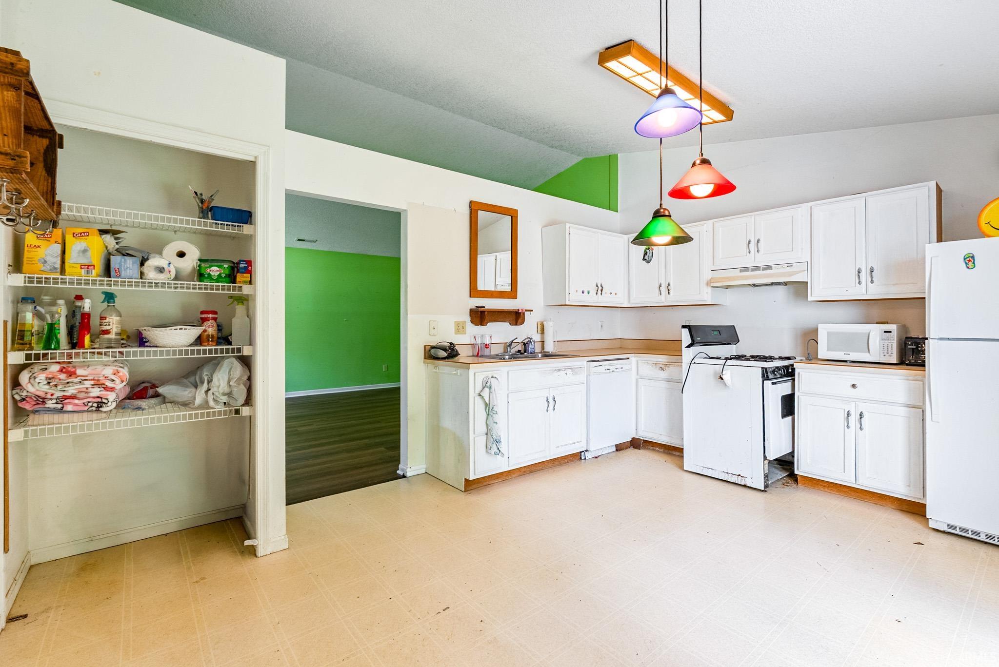 Kitchen featuring white cabinetry, light countertops, and a white appliance suite