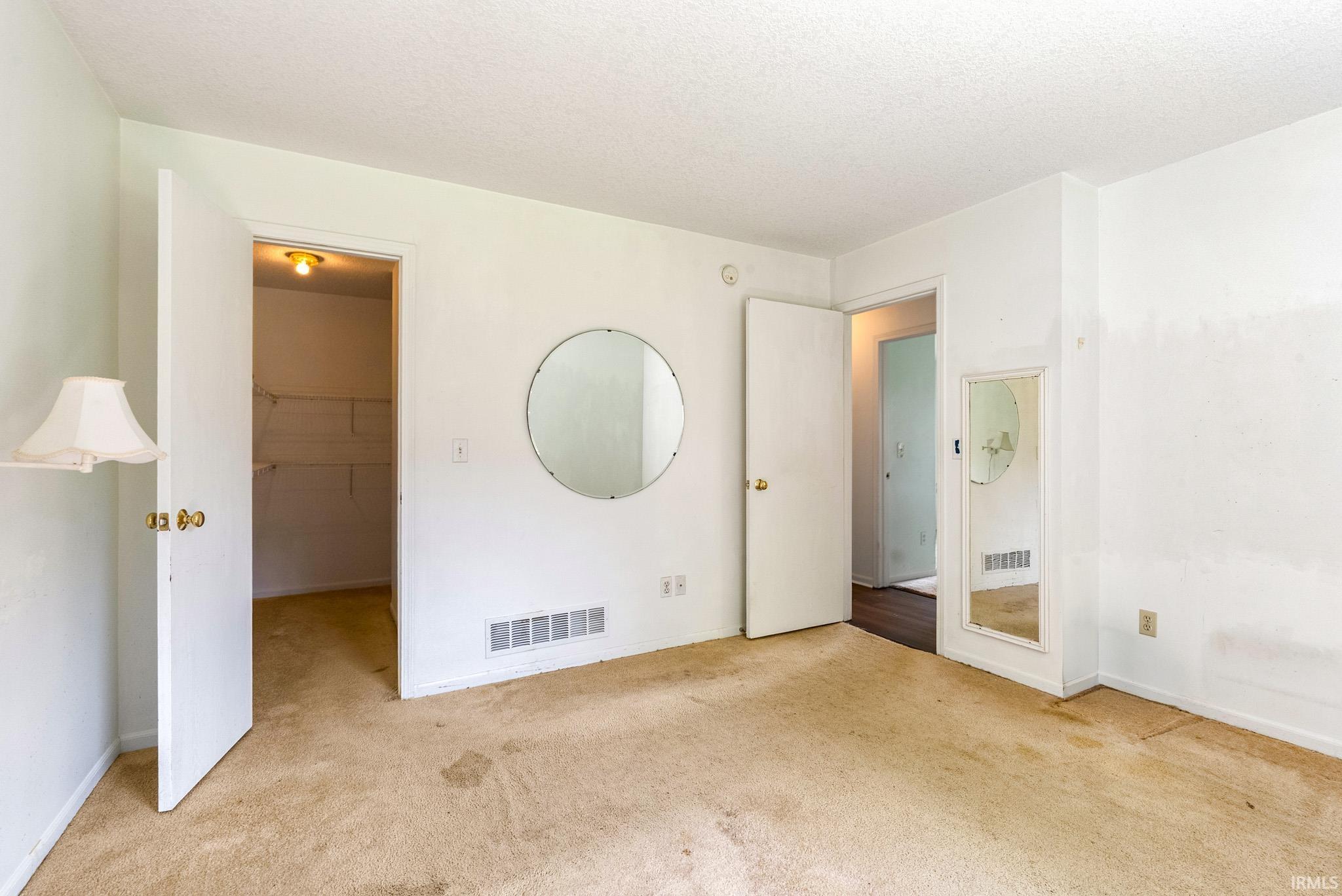 Carpeted room featuring multiple doorways, a built-in closet with shelving, and a wall vent