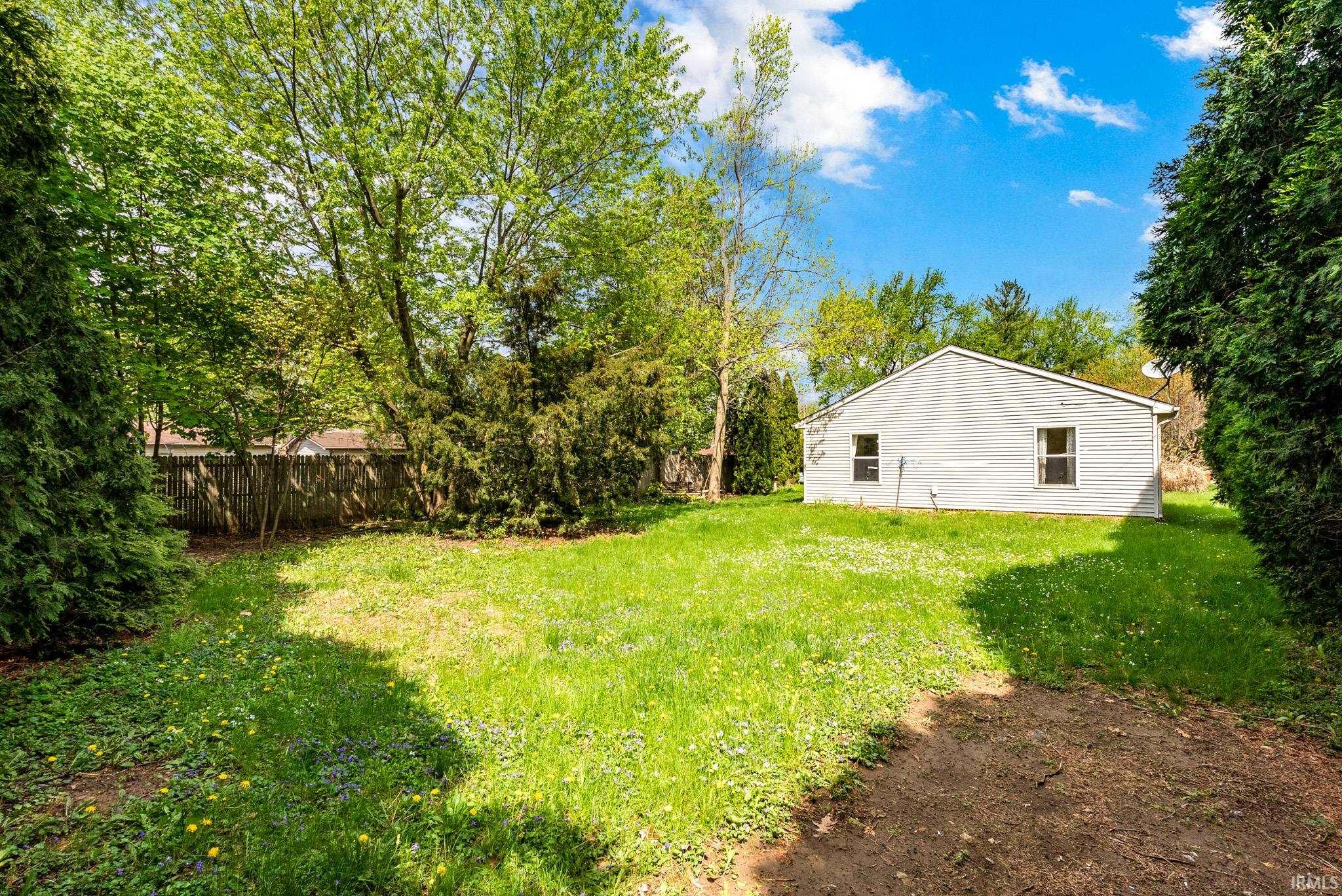 Expansive grassy yard area featuring mature trees and established perimeter plantings