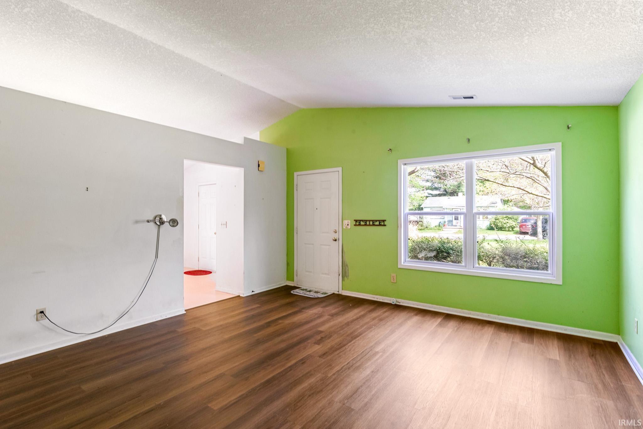 Expansive room featuring wood-finish flooring, a vaulted ceiling, and a large window with white trim