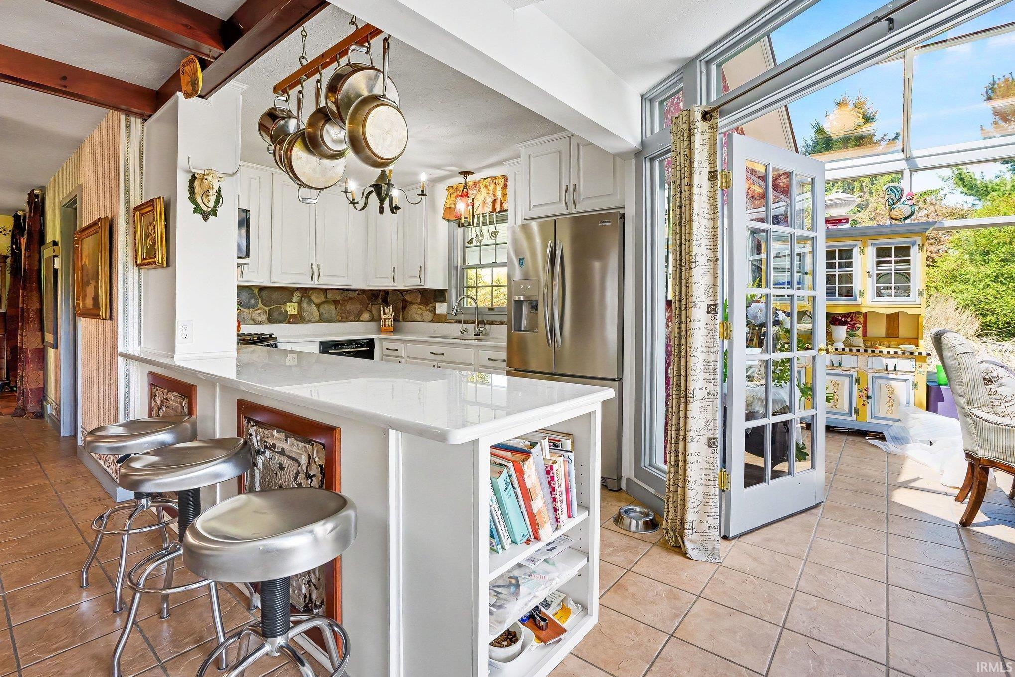 Kitchen featuring white cabinetry, stone-finish backsplash, stainless steel refrigerator, and a breakfast bar with built-in shelving