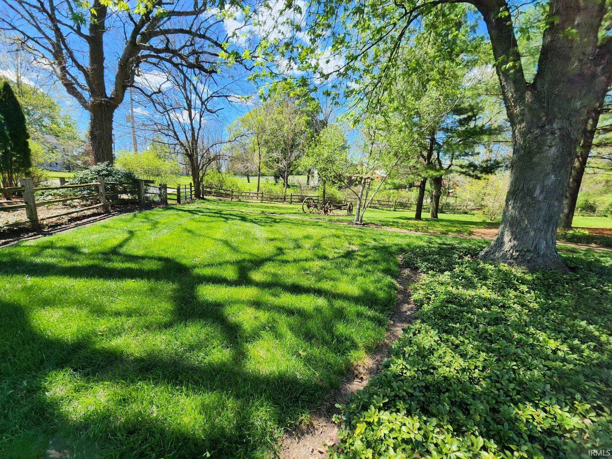 Expansive lawn area featuring mature trees and a rustic split-rail fence