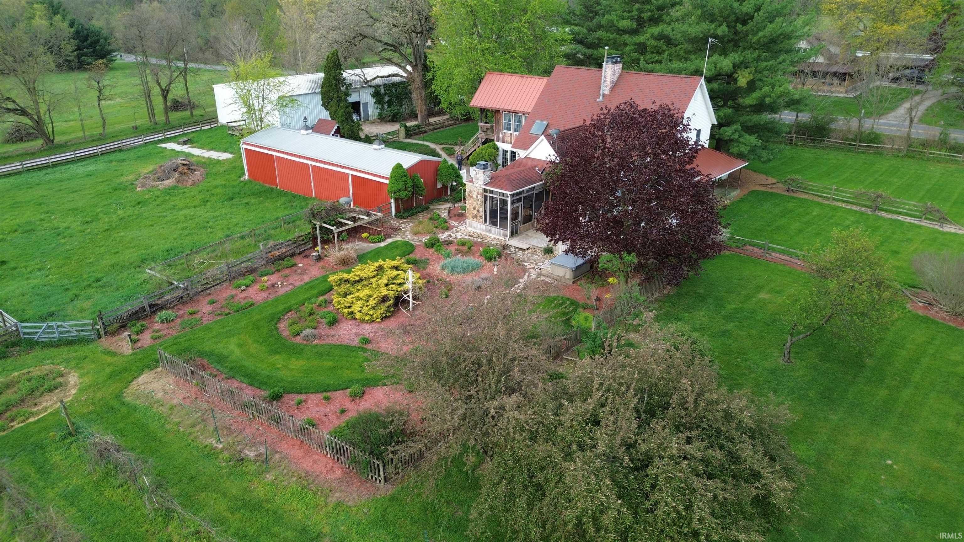 Expansive property featuring a white residence with a red metal roof, a sunroom extension, and a large red barn