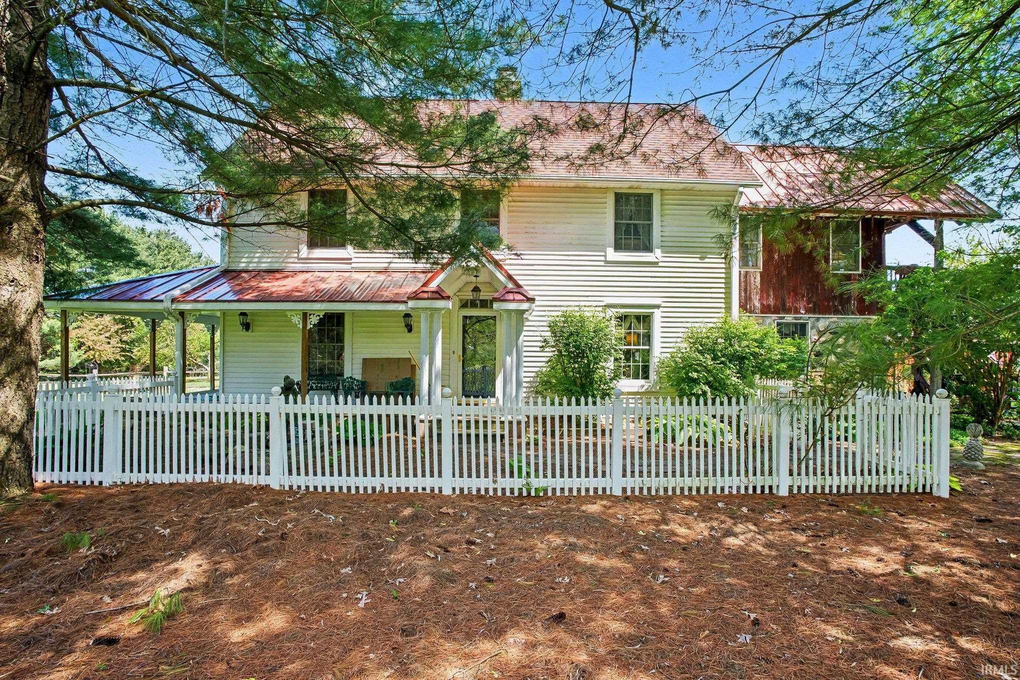 White picket fence framing a classic residence with a red metal roof and a covered porch