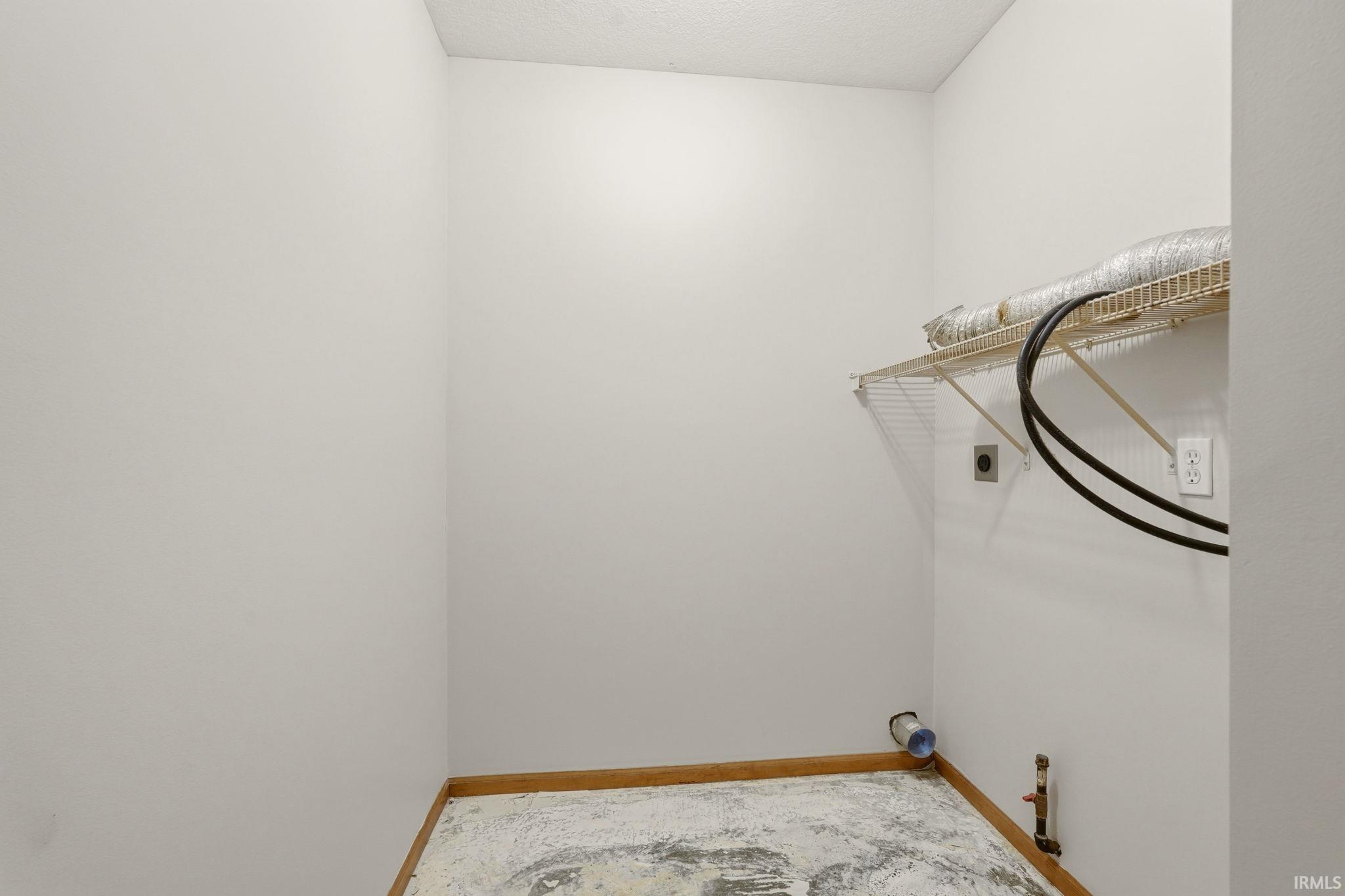 Dedicated utility space featuring a wire shelf, visible electrical outlets, and plumbing hookups