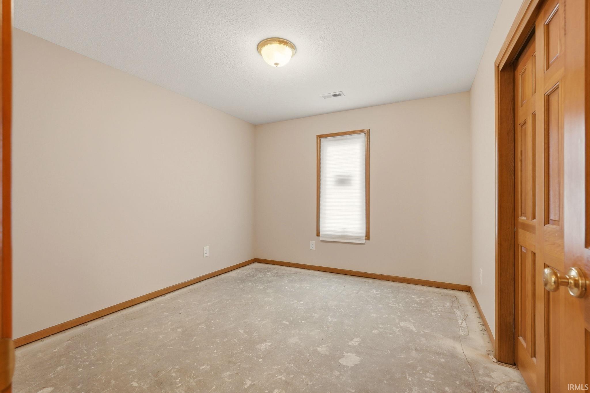 Neutral-toned walls complement a single window with blinds and a warm wood-paneled door