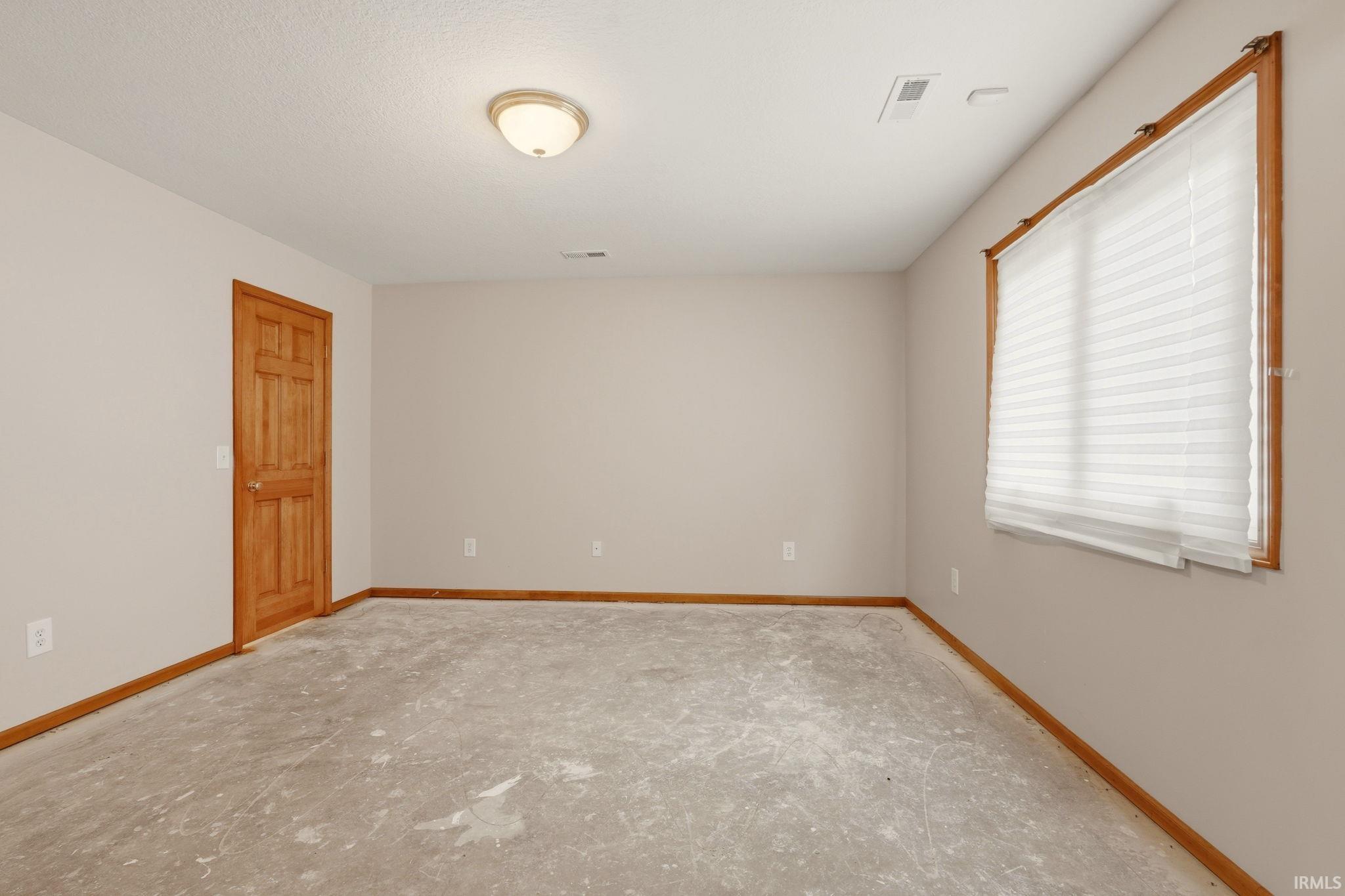 Room featuring light neutral wall paint, wood trim and door, a single window with blinds, and a flush-mount ceiling light fixture