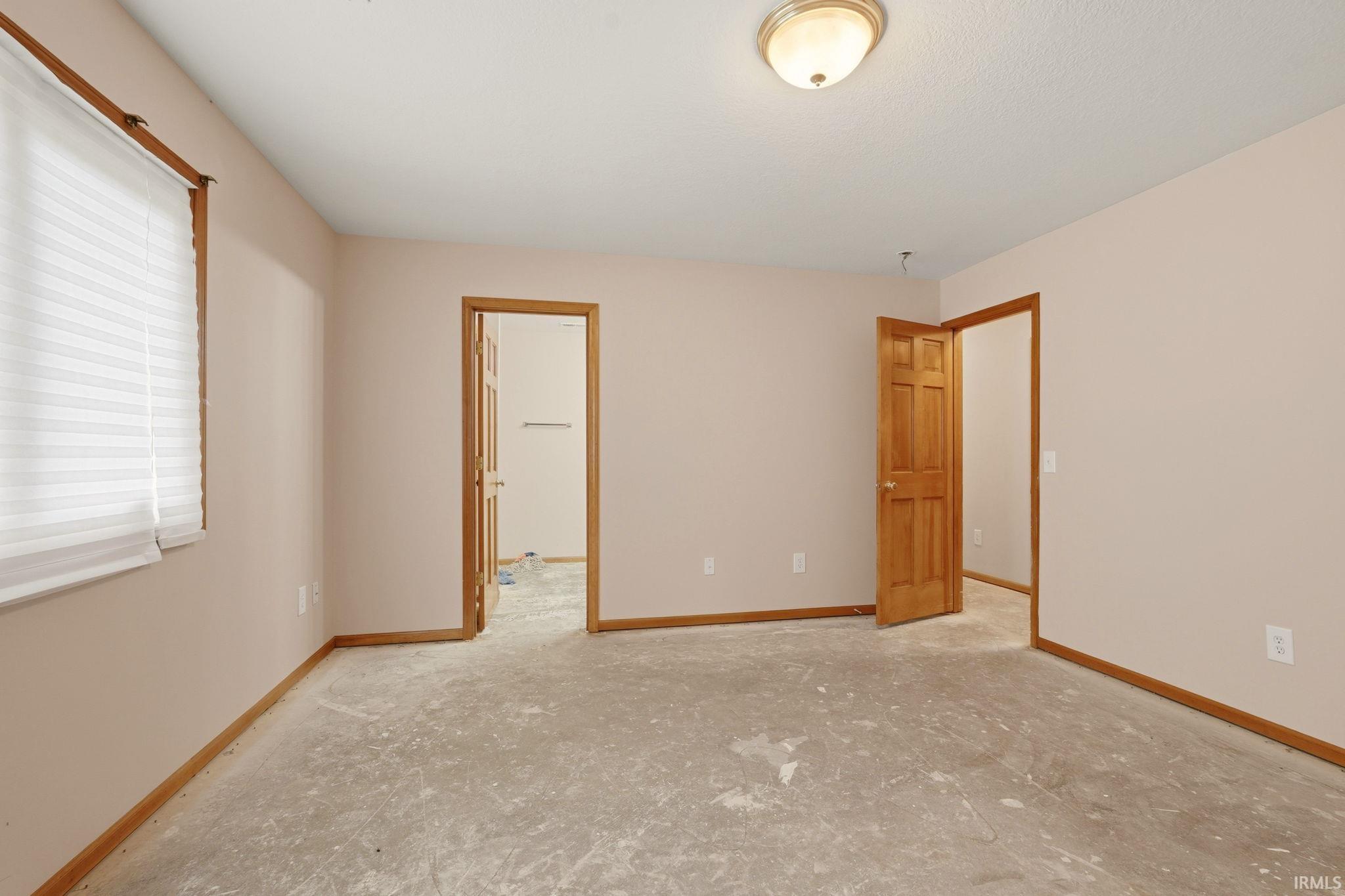 Neutral-toned interior room with exposed subfloor, featuring a window with horizontal blinds and two paneled wood doors