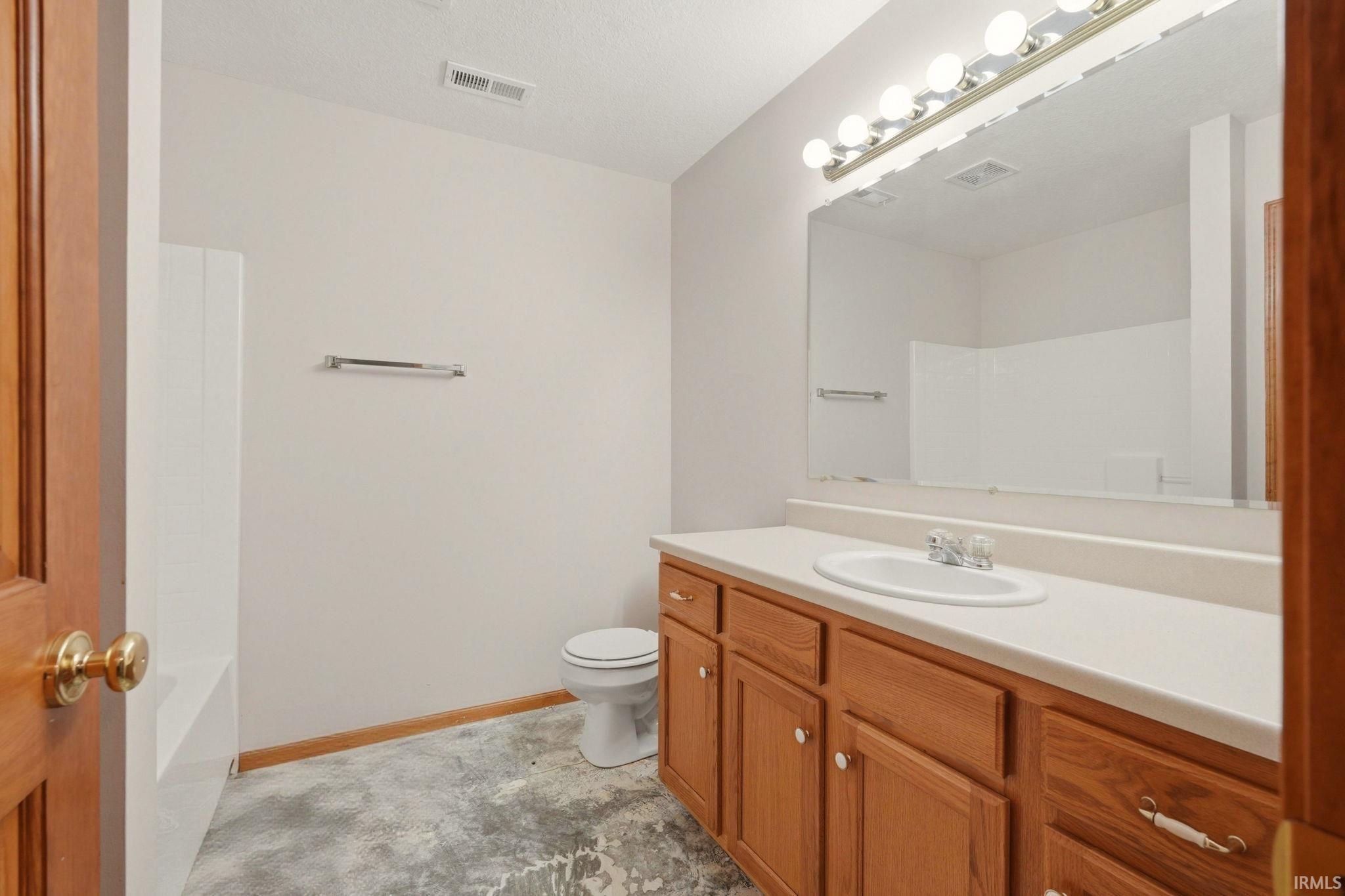 Bathroom featuring a single vanity with wood cabinetry, a large wall-mounted mirror, overhead bar lighting, a toilet, and a combination tub/shower unit