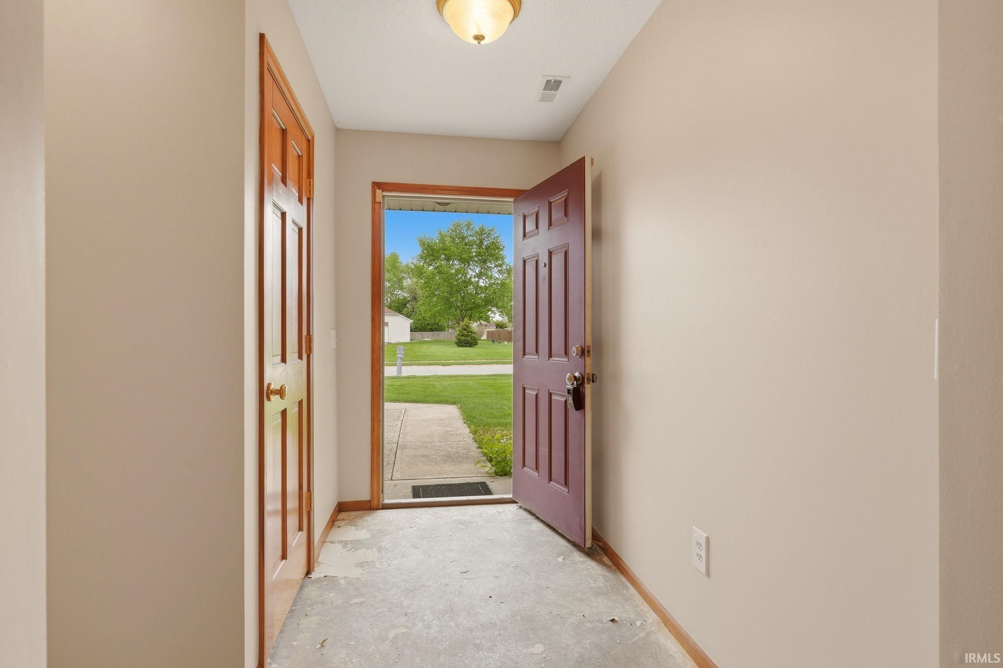 Entryway with a maroon paneled door, light neutral walls, and a warm wood-toned interior door
