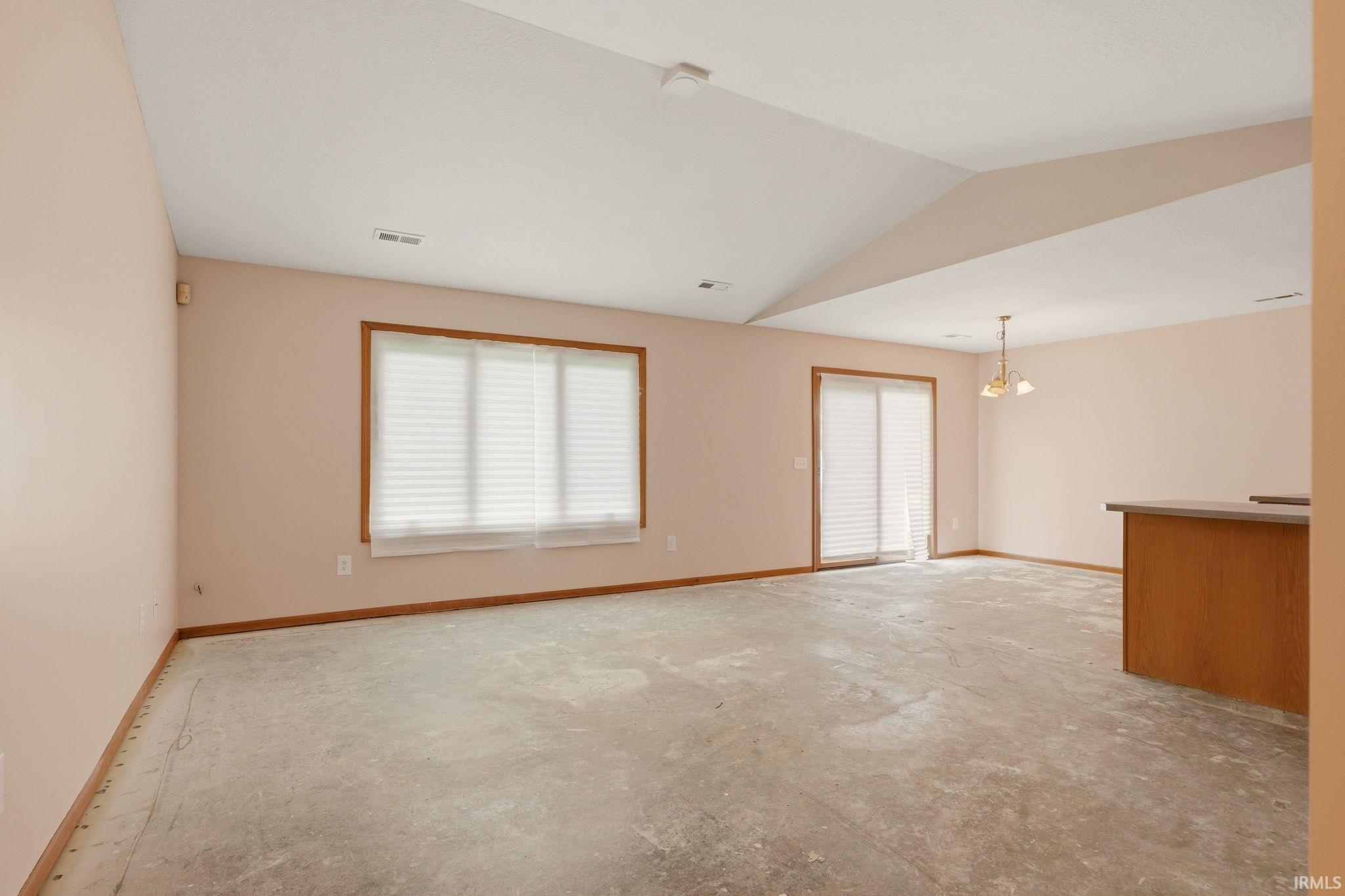 Spacious room featuring a vaulted ceiling and a large window with blinds