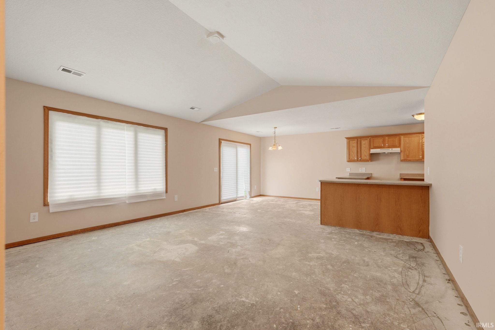 Spacious open-concept area featuring a vaulted ceiling and an abundance of natural light from the large window and sliding glass door