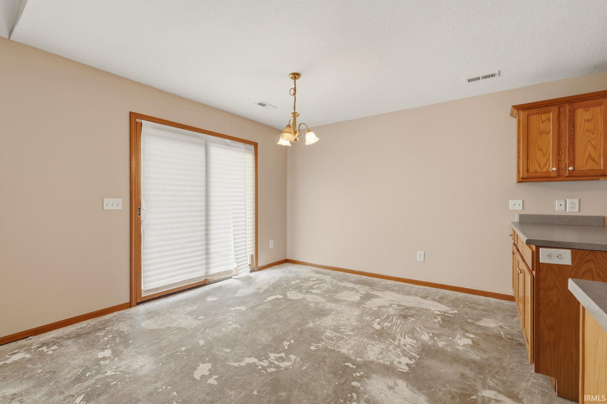 Open-plan area featuring a sliding glass door with horizontal blinds, a ceiling-mounted light fixture, wood-finish cabinetry, and a countertop