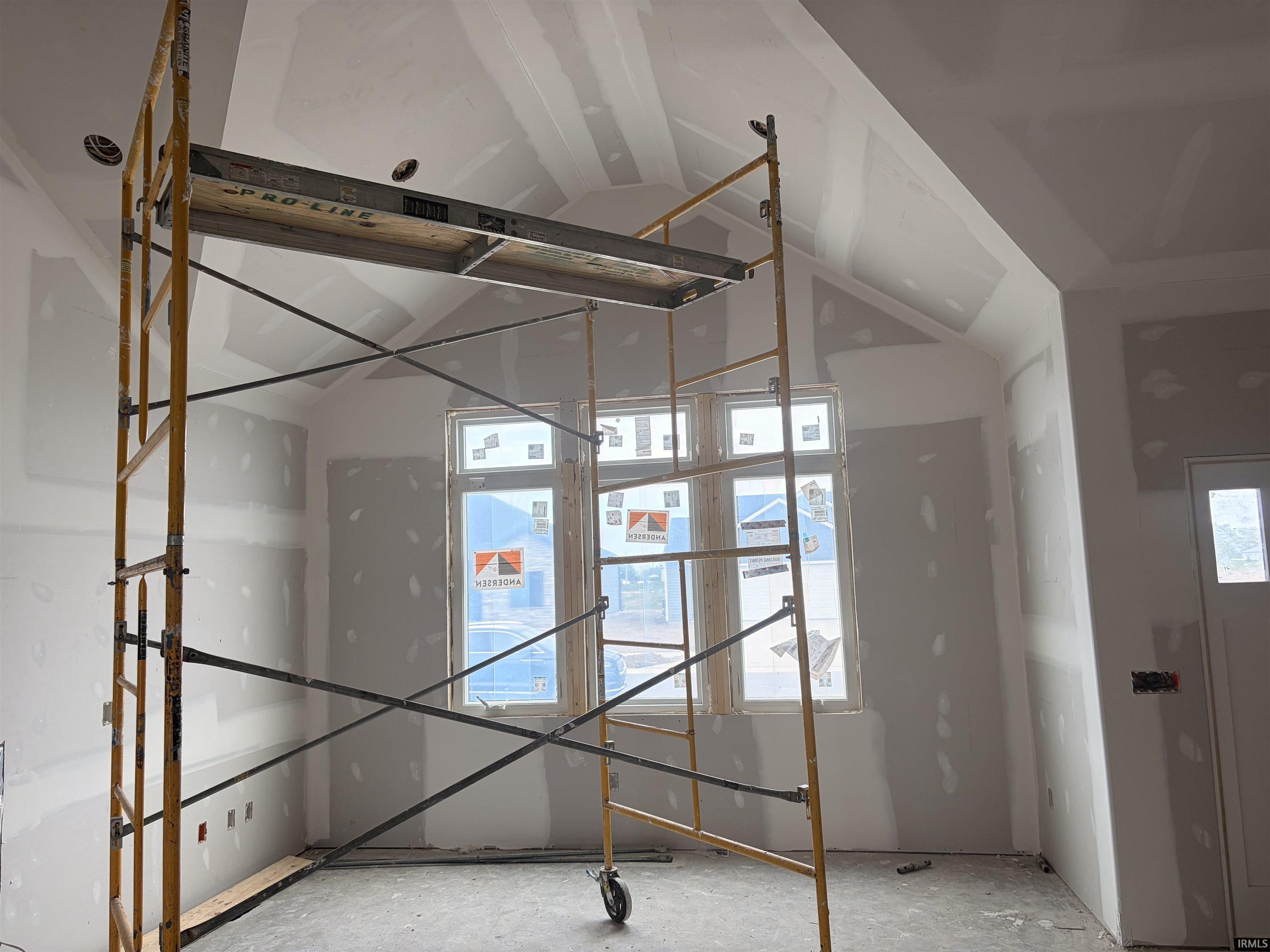 Interior space under construction featuring a vaulted ceiling, multiple windows, and a partially finished door frame