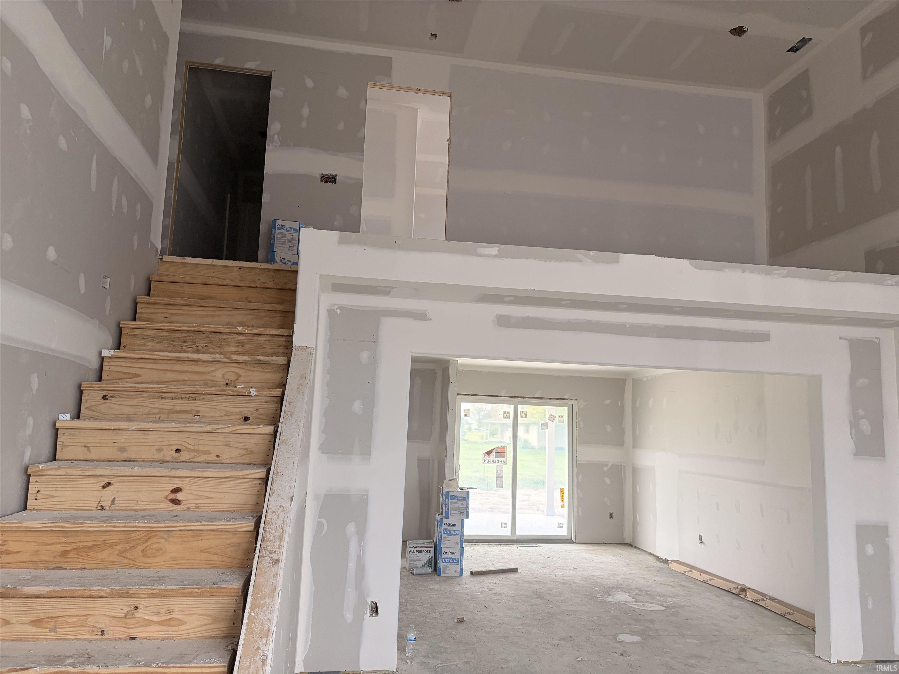 Interior construction showcasing unfinished wood stairs, drywall, and a framed archway