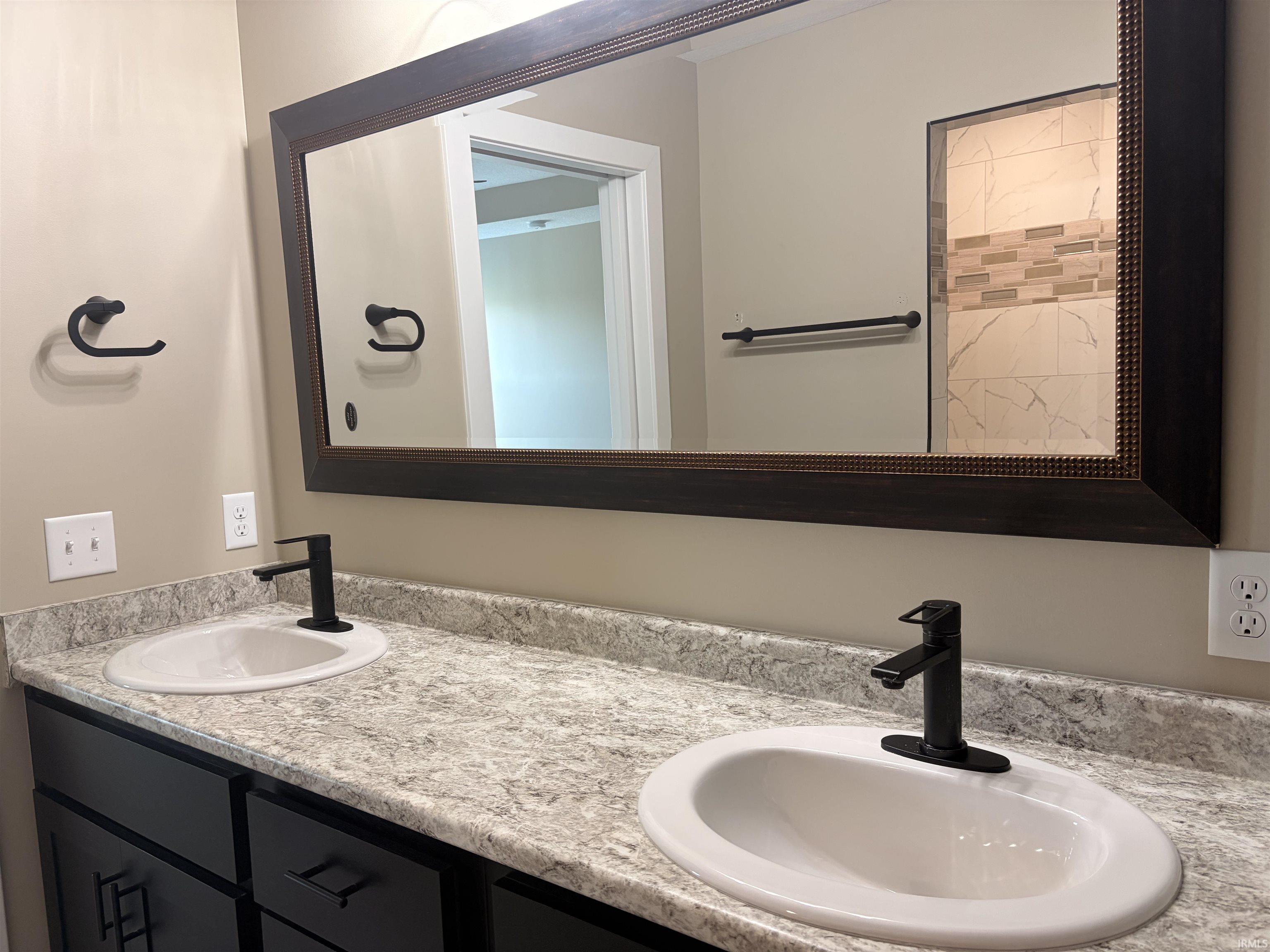 Dual vanity featuring dark cabinetry, speckled countertops, and matte black fixtures