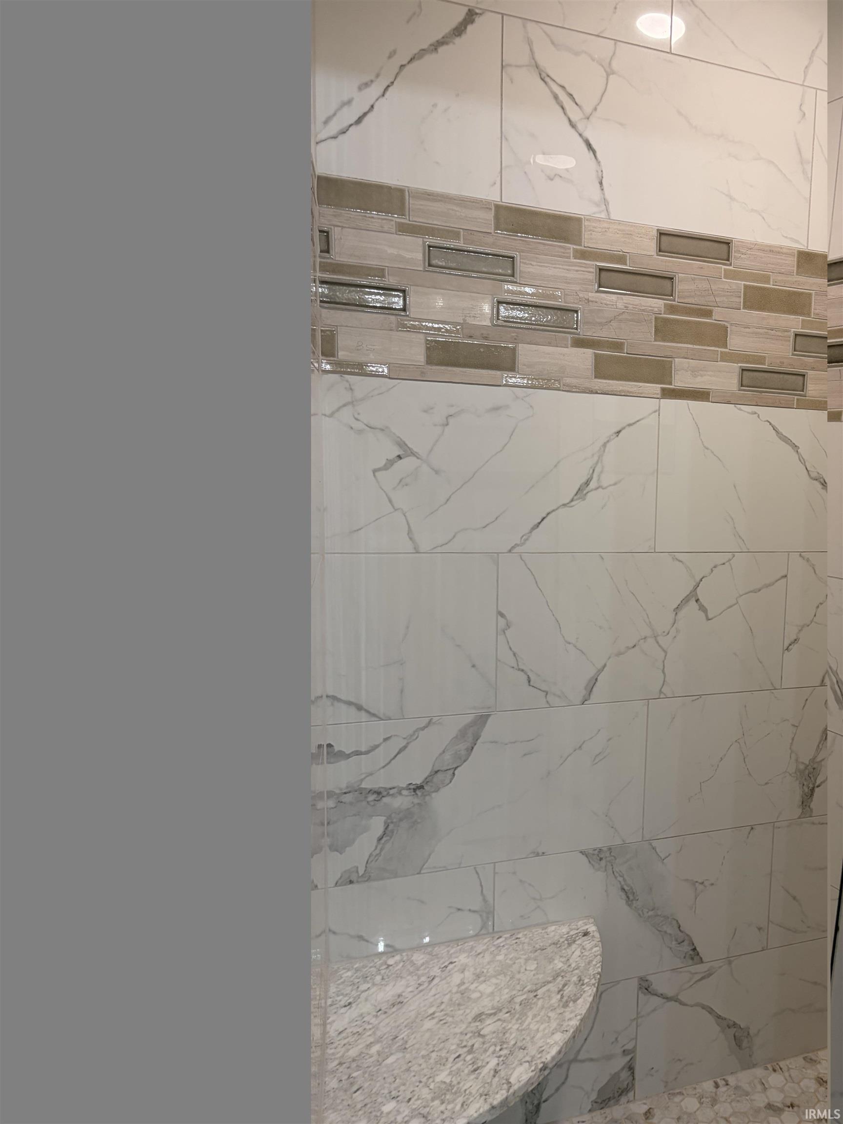 White tile shower surround with grey veining, accented by a decorative mosaic band