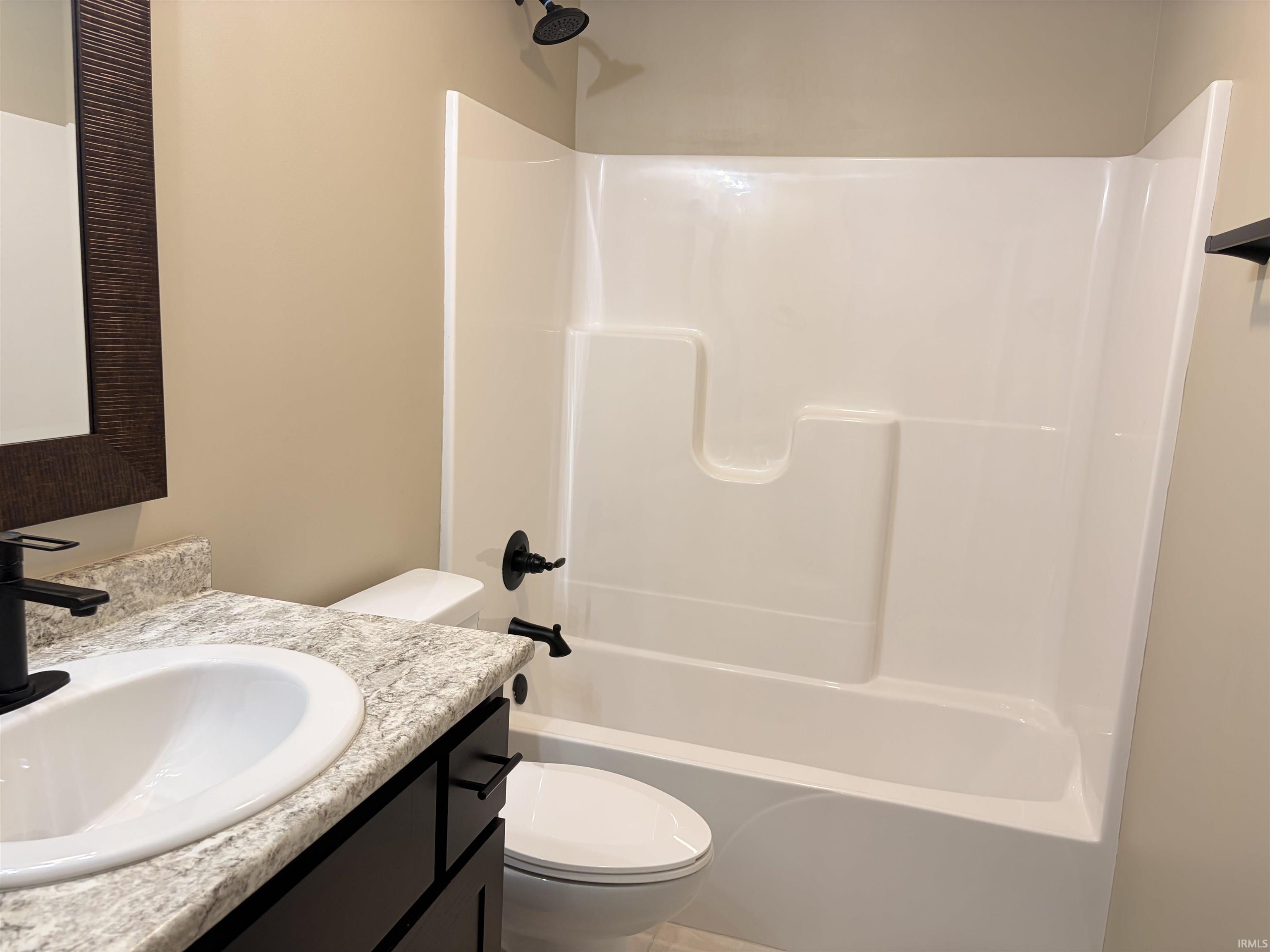 Bathroom featuring a white integrated tub and shower unit with matte black fixtures, a white oval sink set in a light granite-look countertop, a dark wood-finish vanity with matte black hardware, and a framed mirror