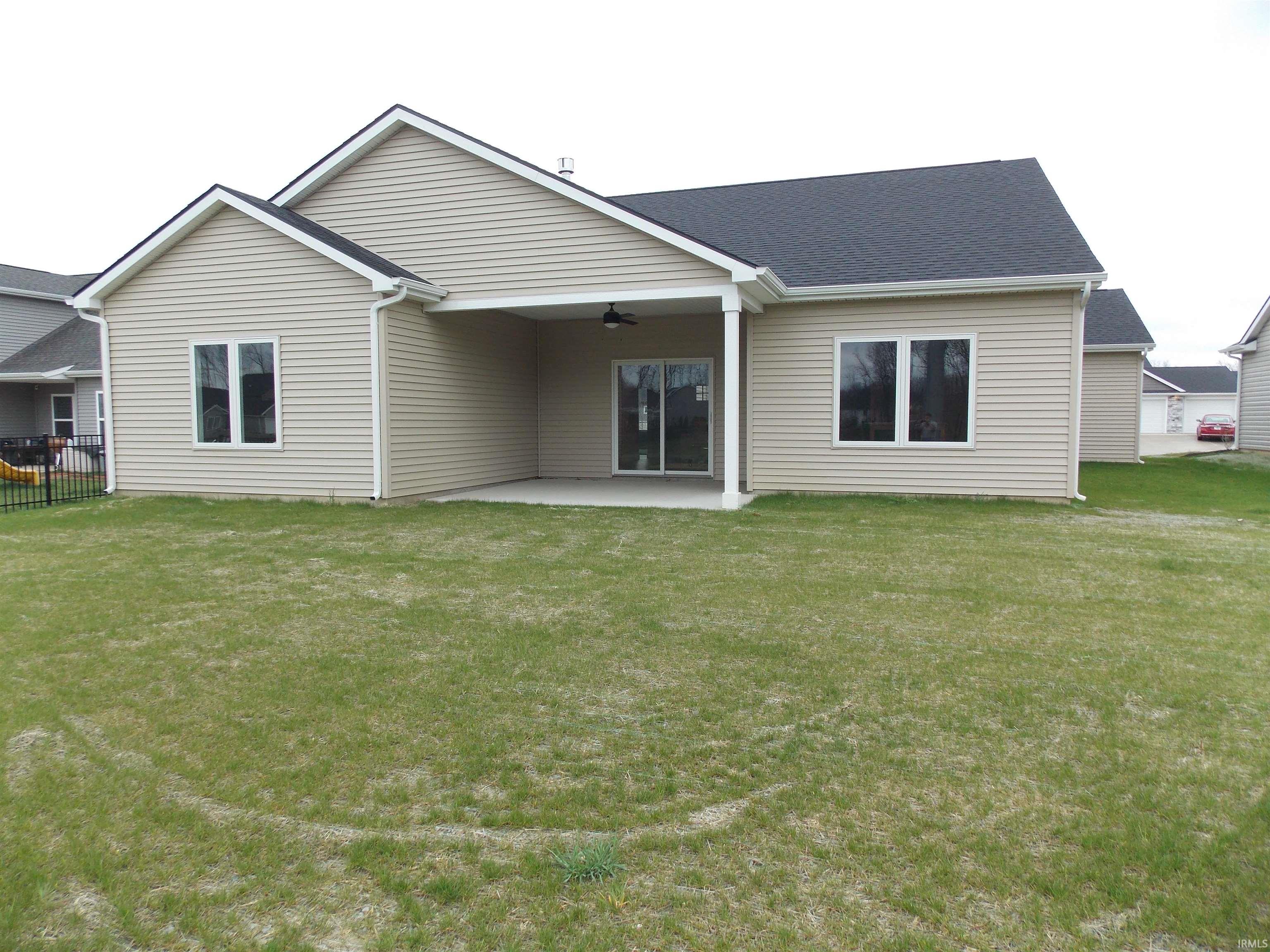 Rear exterior featuring tan horizontal siding, a covered concrete patio, and a dark shingle roof
