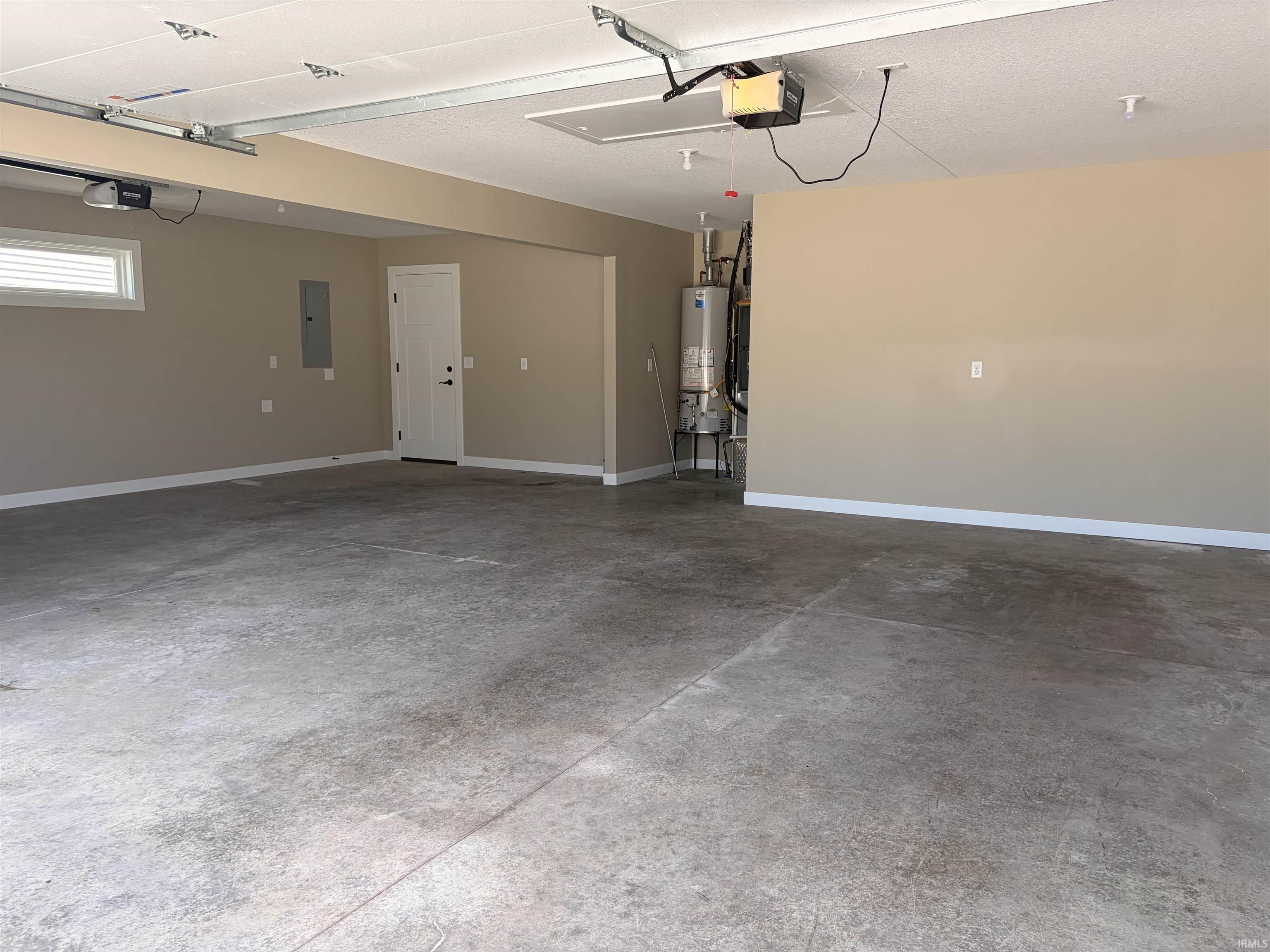 Spacious garage with concrete flooring, a single window, a white interior door, a water heater, and an electrical panel