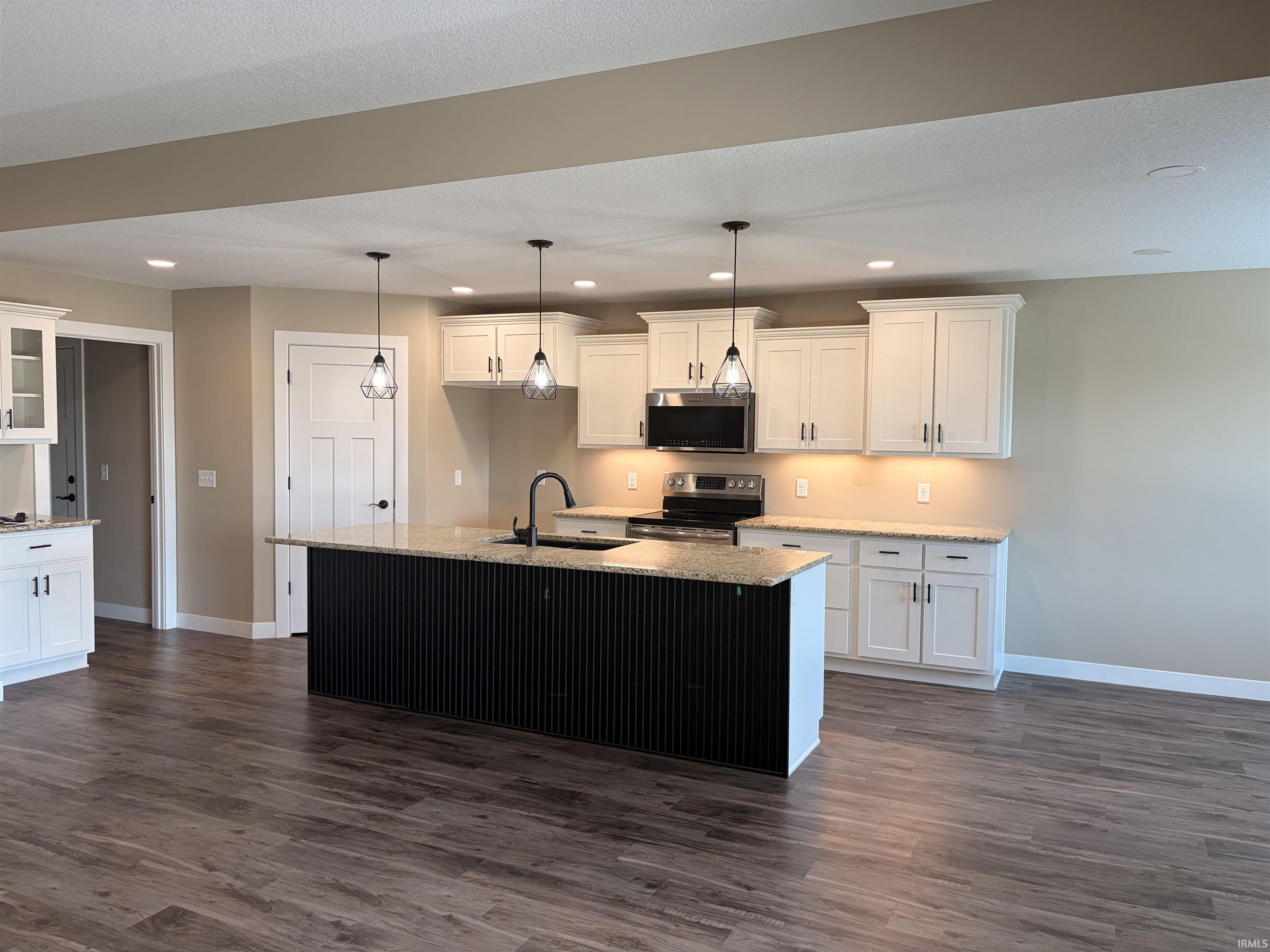 Open-concept kitchen featuring a large black island with a light-toned countertop, white cabinetry with dark hardware, a full suite of stainless steel appliances, and wood-finish flooring