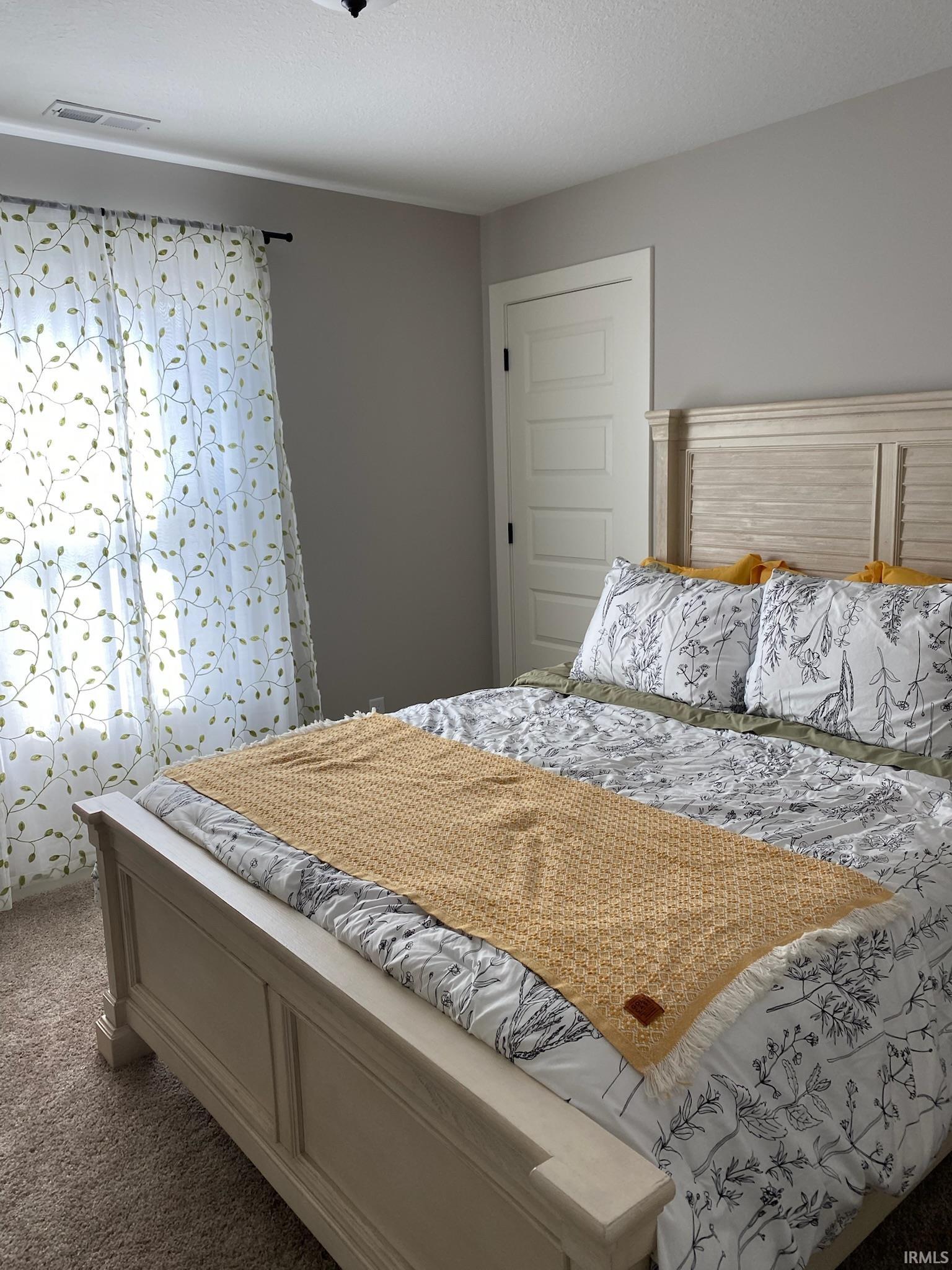 Carpeted bedroom featuring a light-colored wood-finish bed frame with a slatted headboard