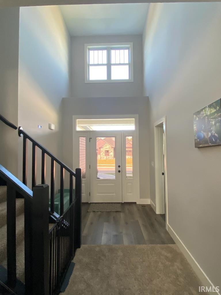 Two-story entryway featuring a transom window, wood-finish flooring, a white paneled front door with side lites, and a staircase with dark balusters