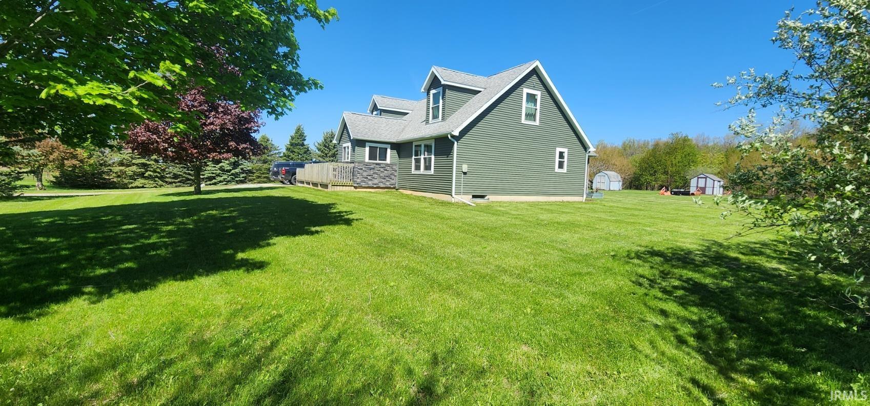 Expansive green lawn surrounds a two-story residence featuring dormer windows, green siding, and a wooden deck