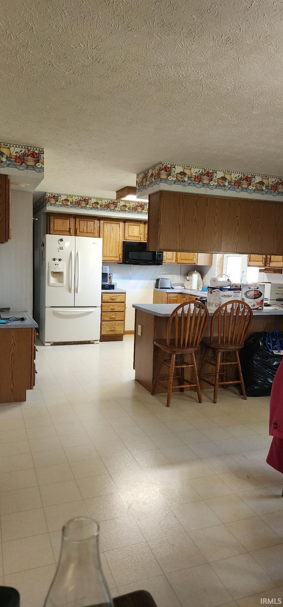 Kitchen featuring light wood cabinetry, white appliances, and a central island with bar seating