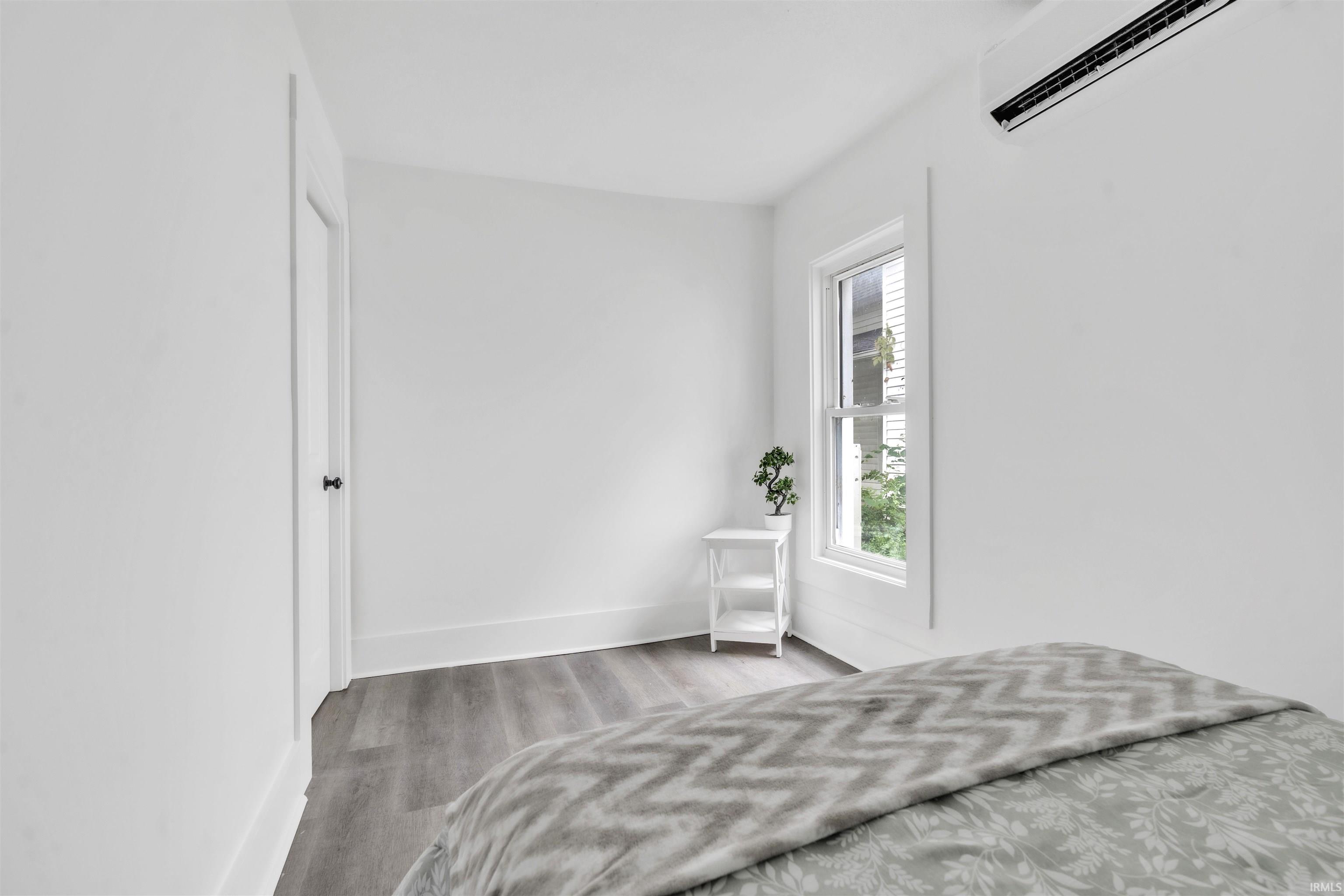 Room featuring neutral wall tones, wood-finish flooring, a white-framed window, and a wall-mounted mini-split system