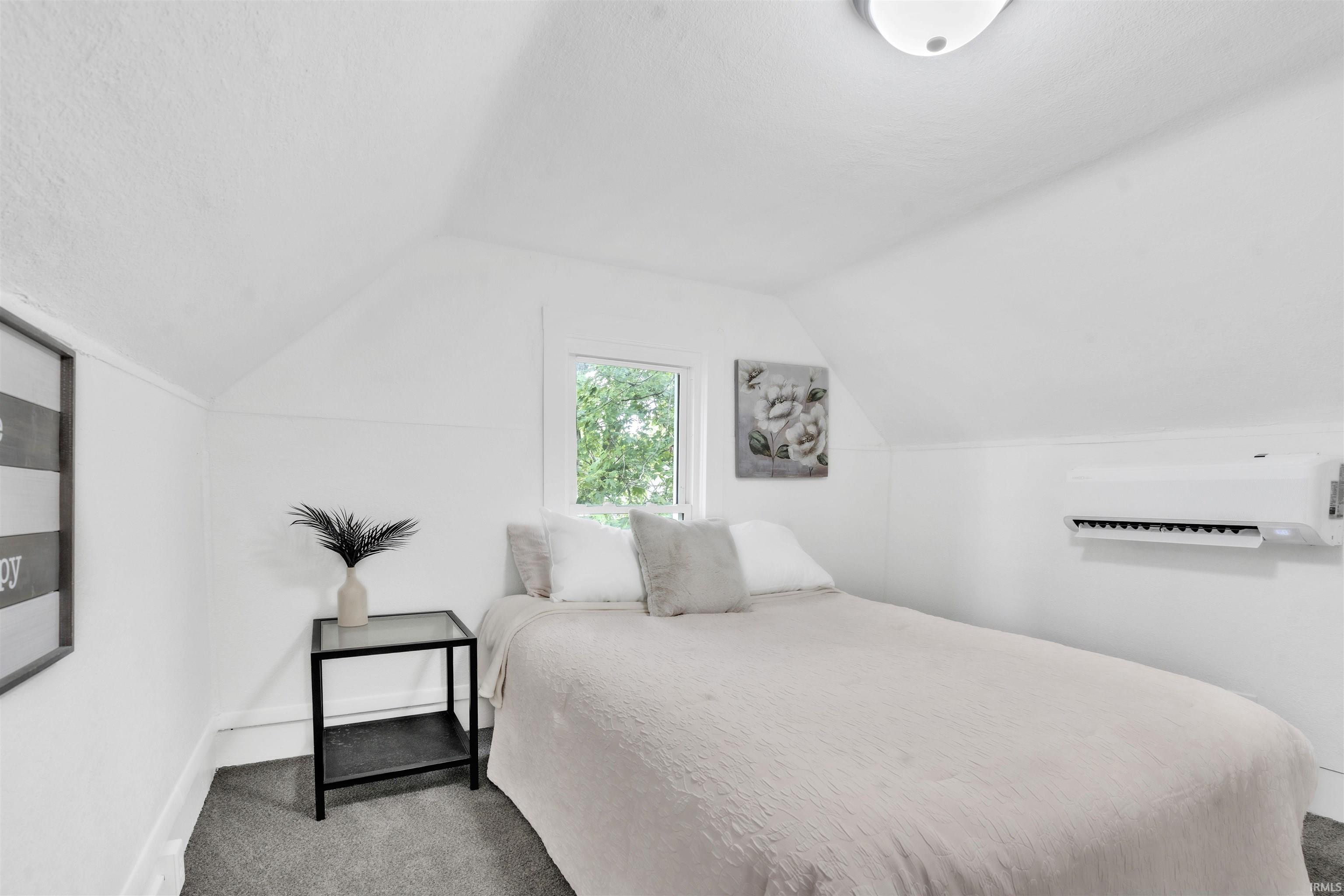 White painted walls with sloped ceiling accents, recessed window, dark gray carpeting, and a wall-mounted climate control unit